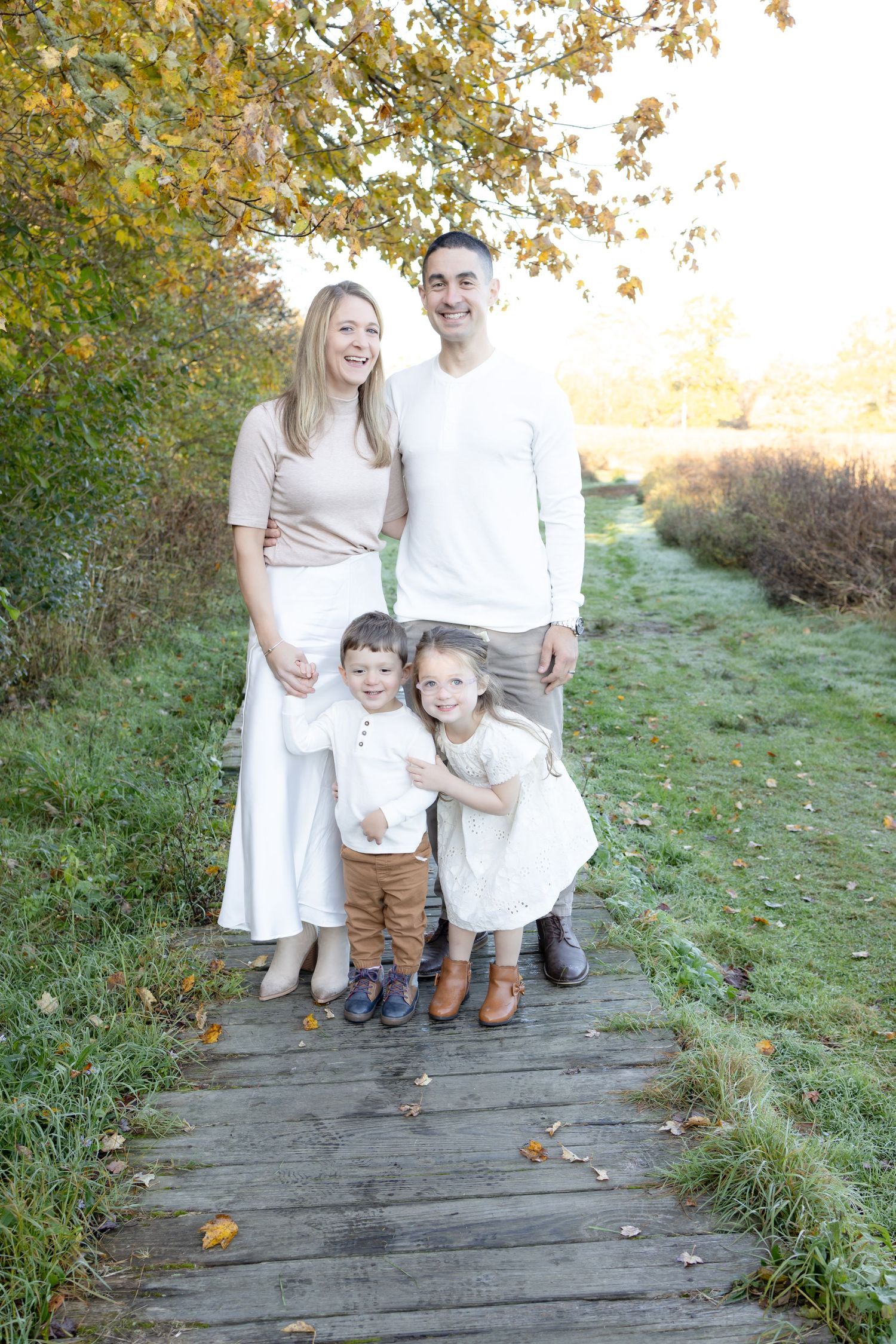 Family standing together on wooden path surrounded by autumn foliage.