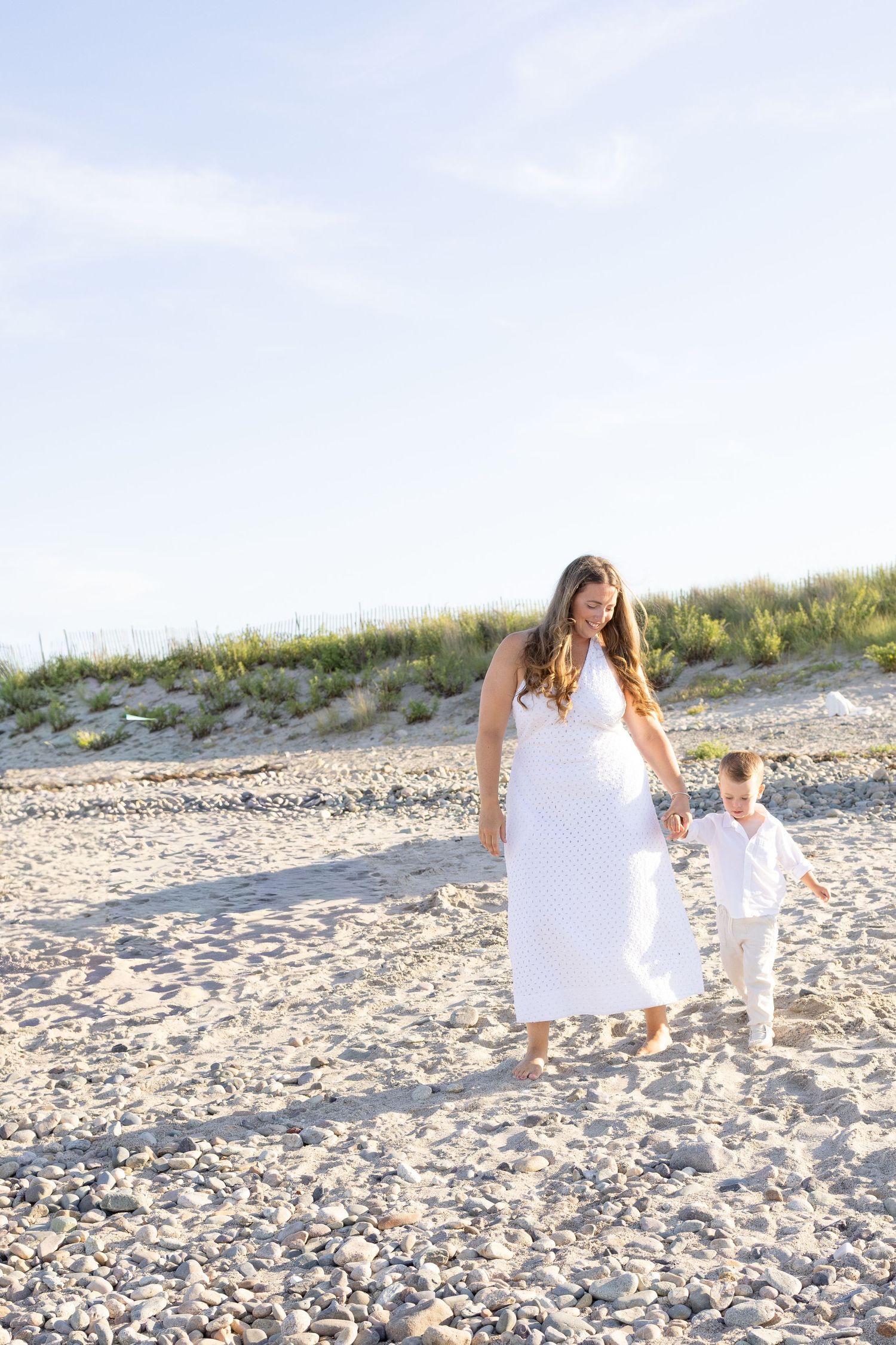 Mother and child walking together on sunny beach.
