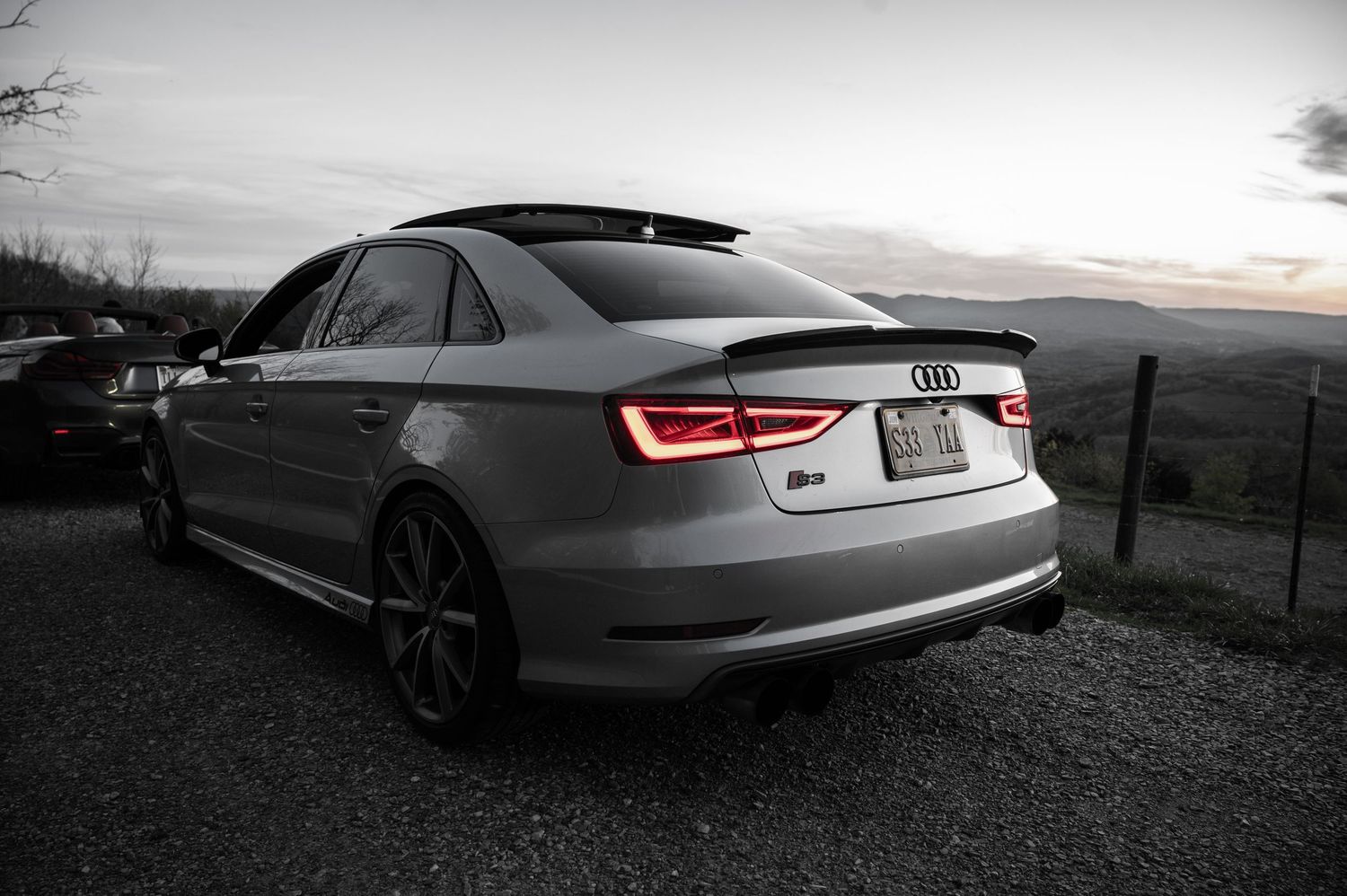 Sleek silver Audi S3 sedan with glowing LED taillights parked at dusk against a moody black and white landscape.