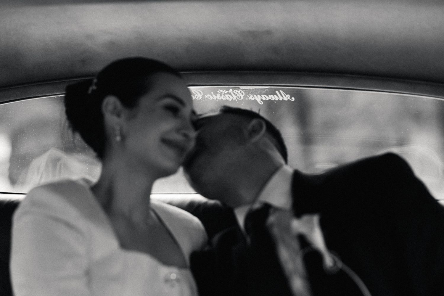 Candid black and white photo of newlyweds sharing a quiet moment in their wedding car.