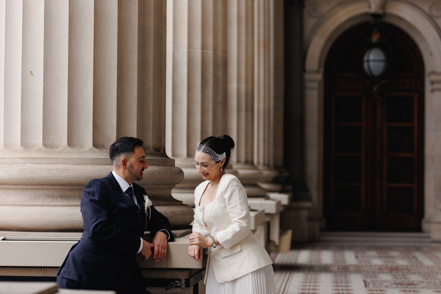 Newlyweds sitting together outside a Melbourne building during their wedding portraits.