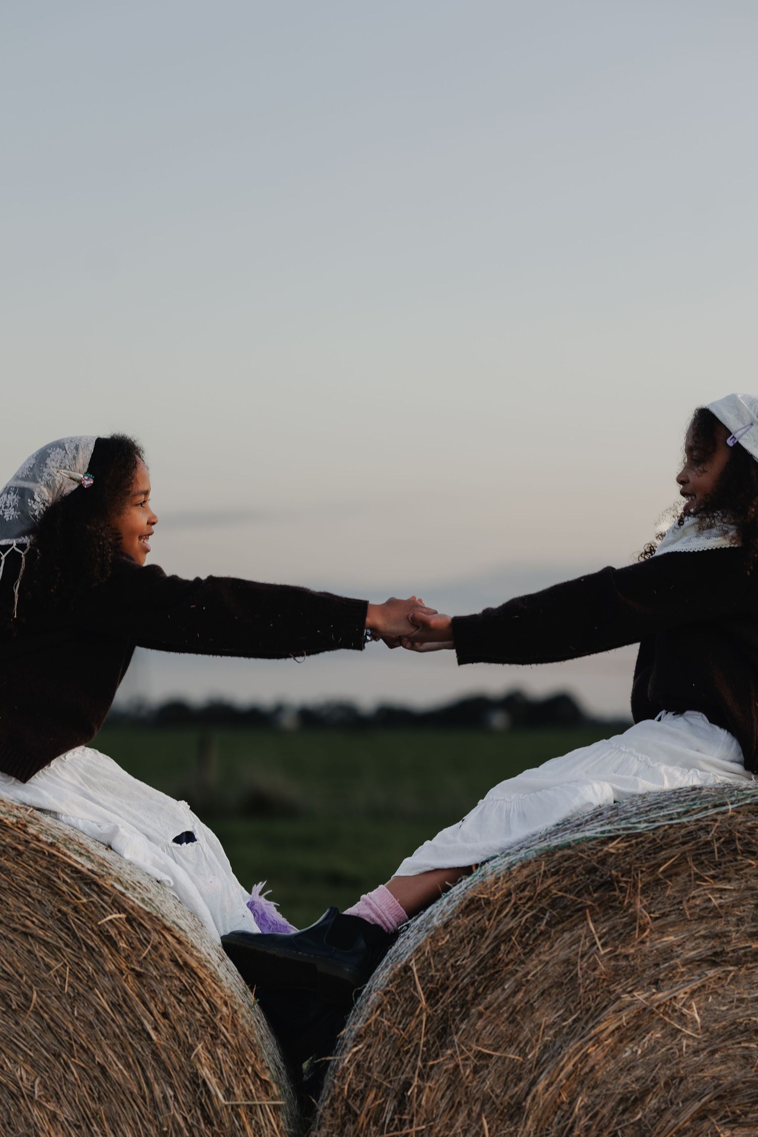 Two family members reaching for each other while sitting on hay bales outdoors.
