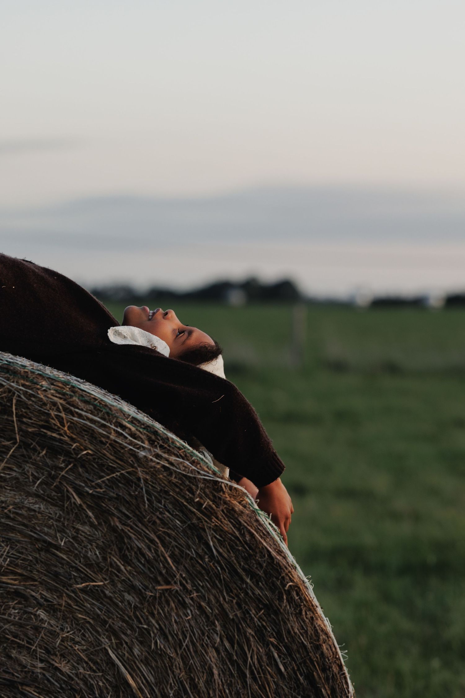 Candid child resting against a hay bale during a documentary-style family photo session.