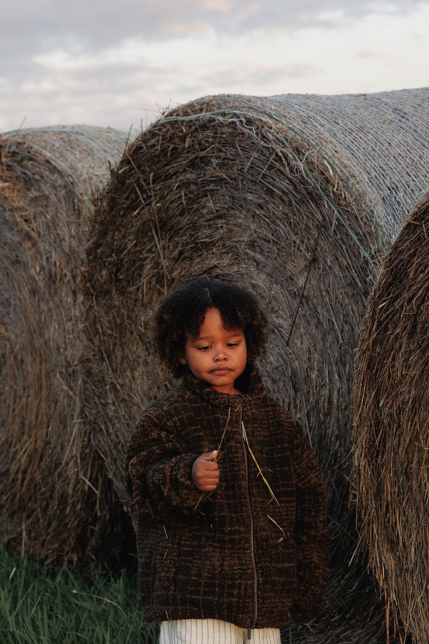 Child standing beside hay bales during an outdoor family photography session.