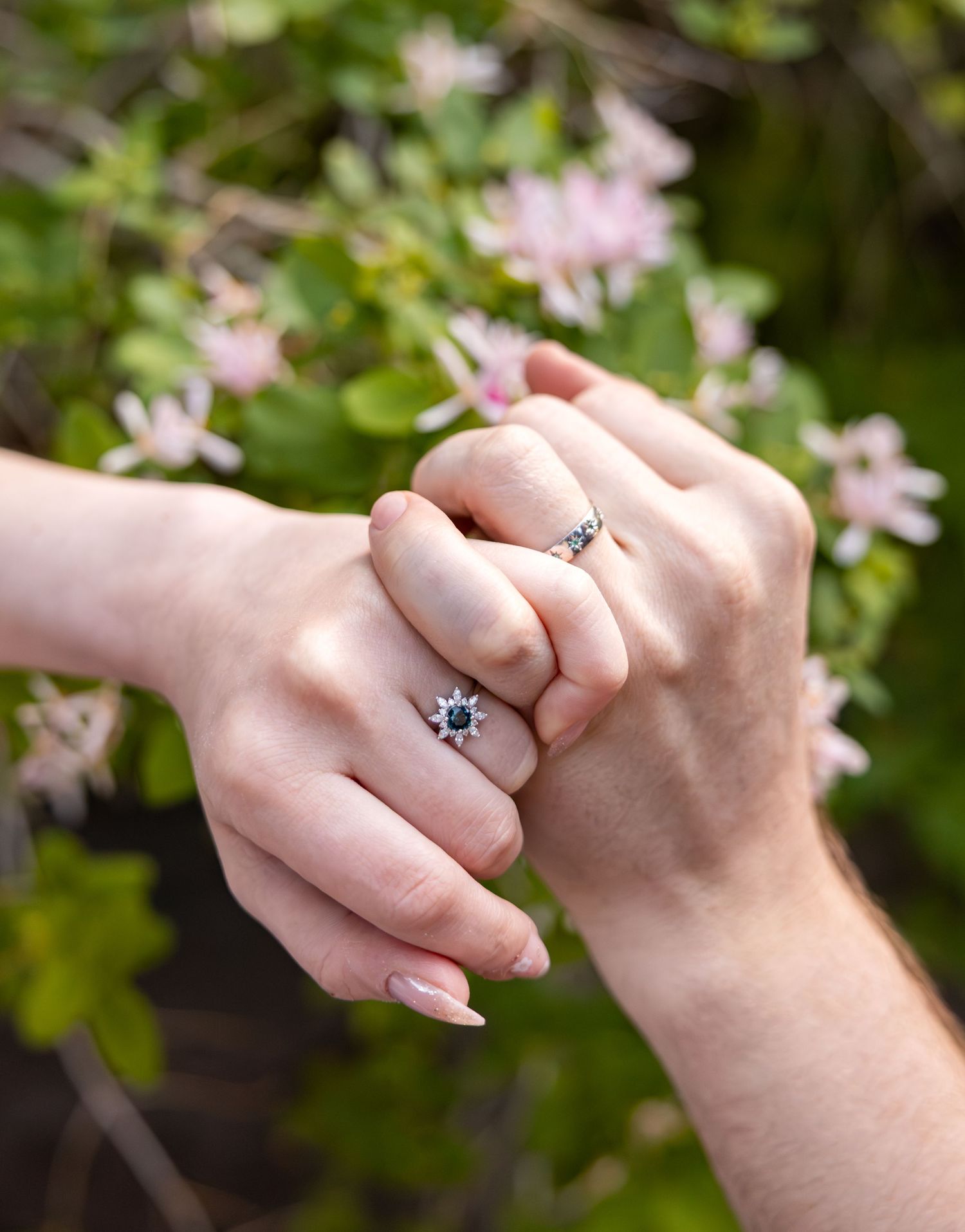 A newly engaged couple interlock their pinky fingers to show off their engagement rings.