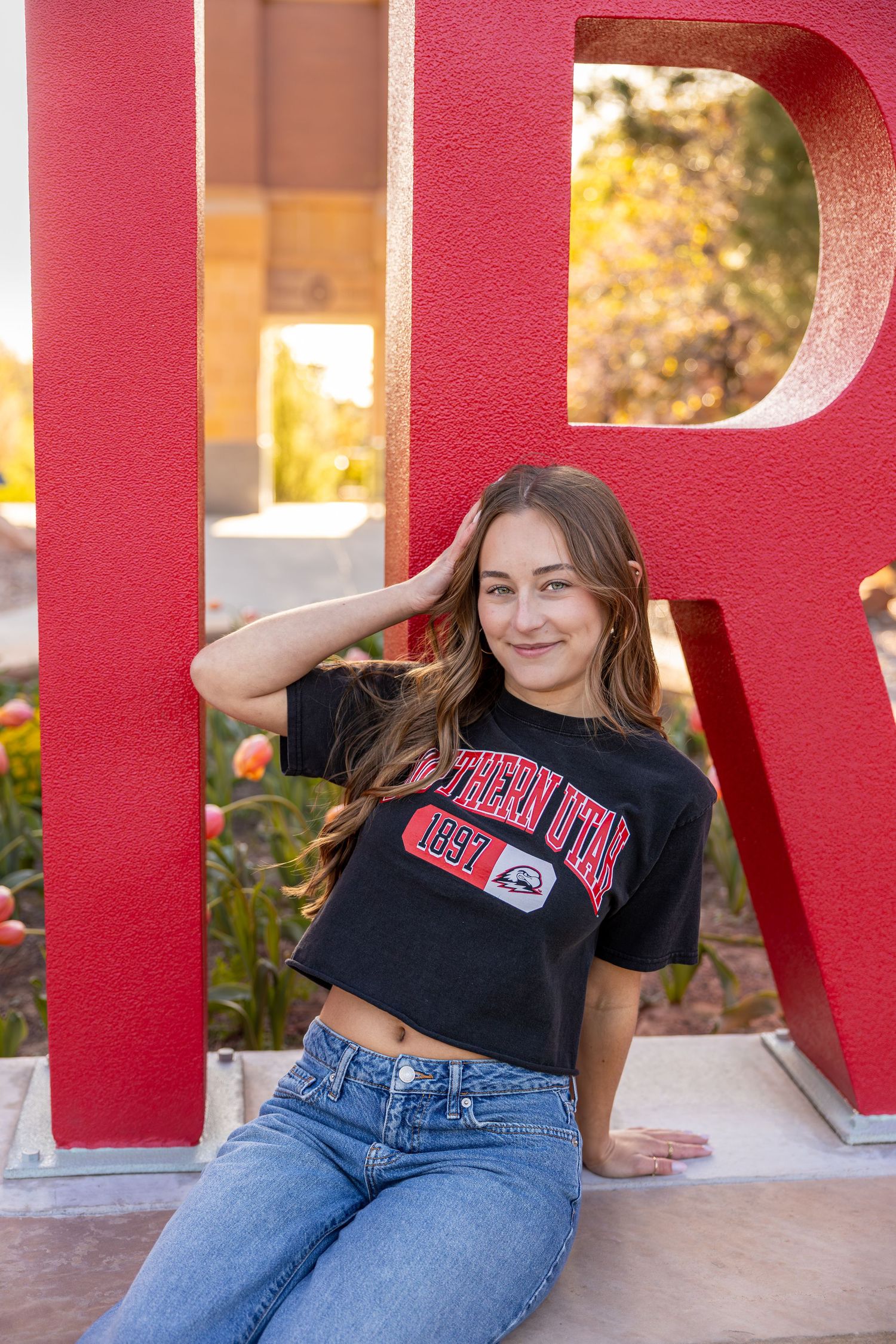 A college graduate is sitting in front of the TBirds sign at the SUU Campus in Cedar City, Utah.