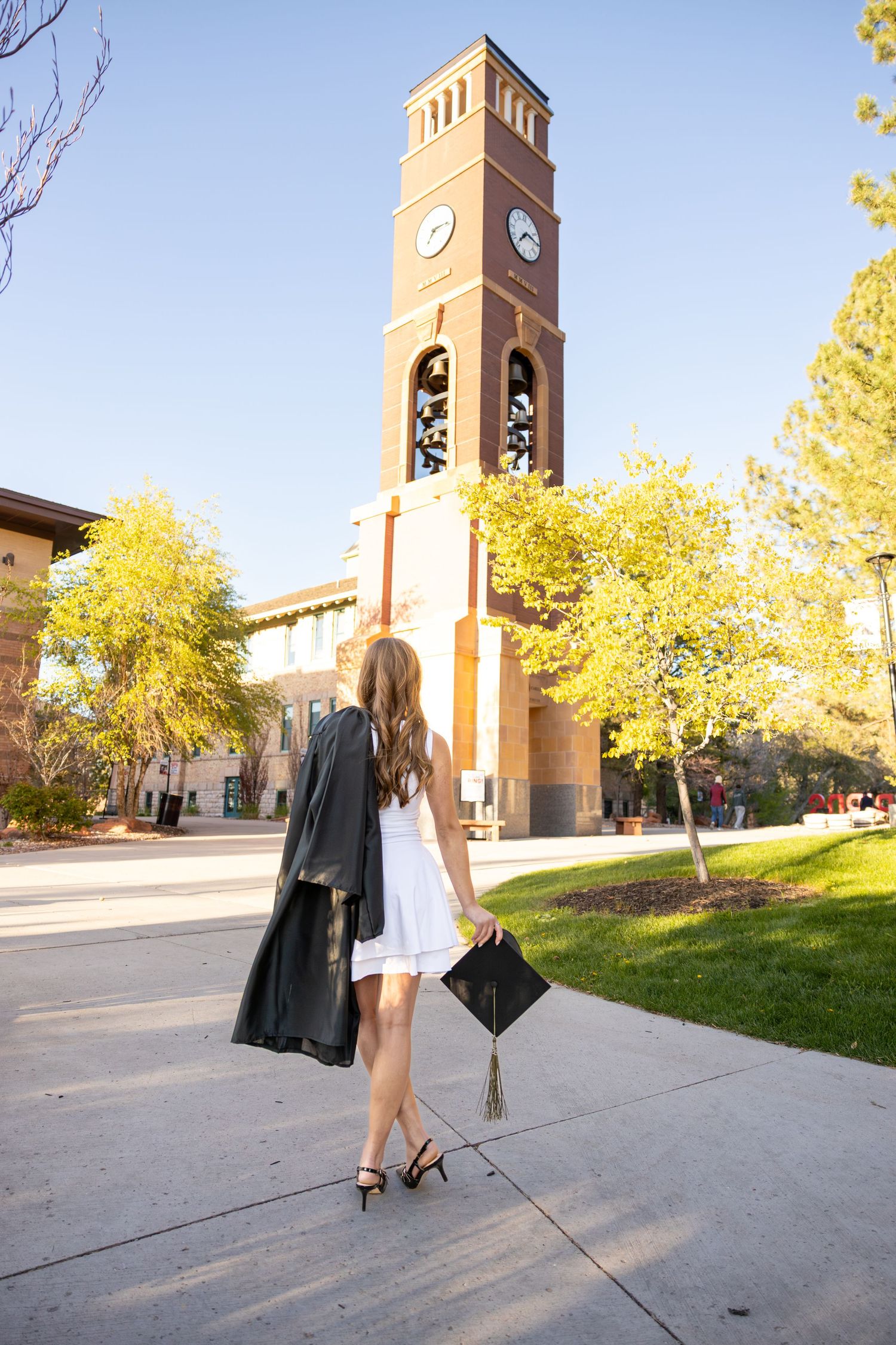 A college graduate is holding her cap in front of the SUU Bell Tower in Southern Utah.
