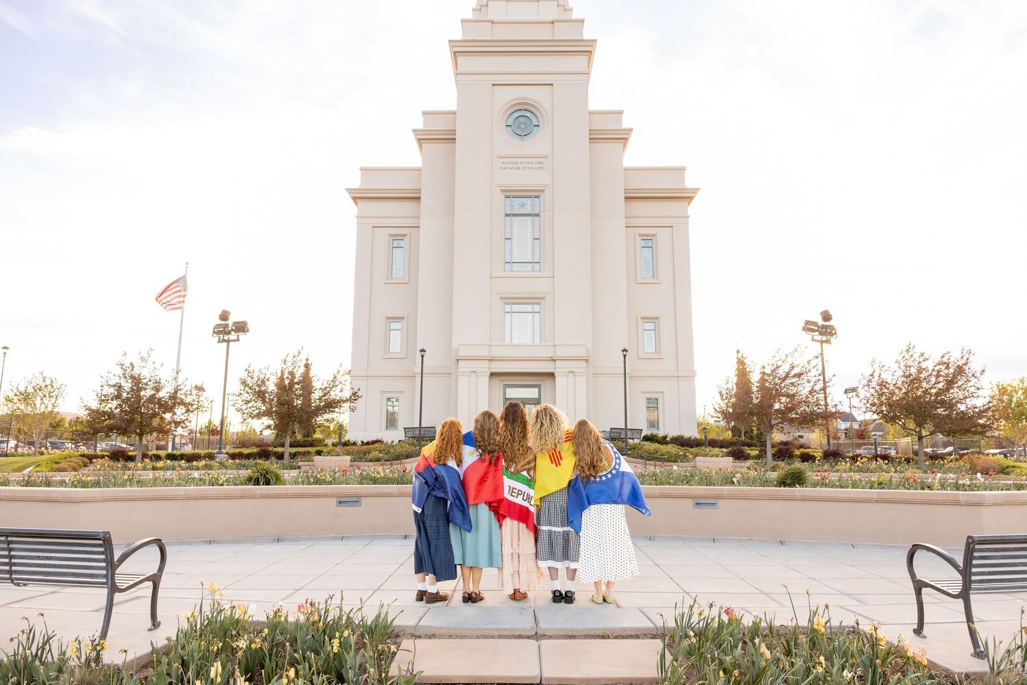 5 girls are standing in front of the Cedar City LDS temple with their mission flags wrapped around them.