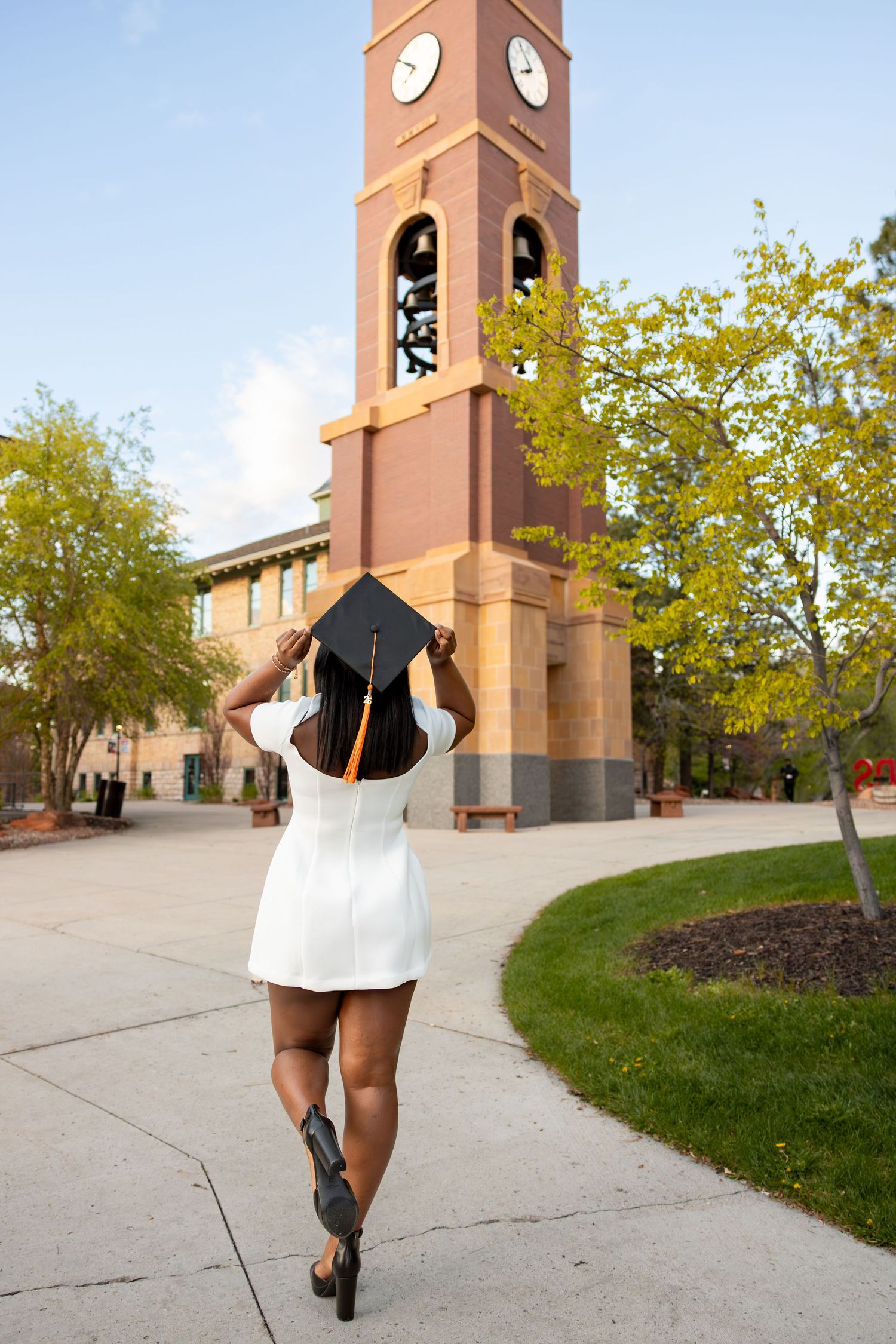 A college graduate is holding her cap in front of the SUU Bell Tower in Southern Utah.
