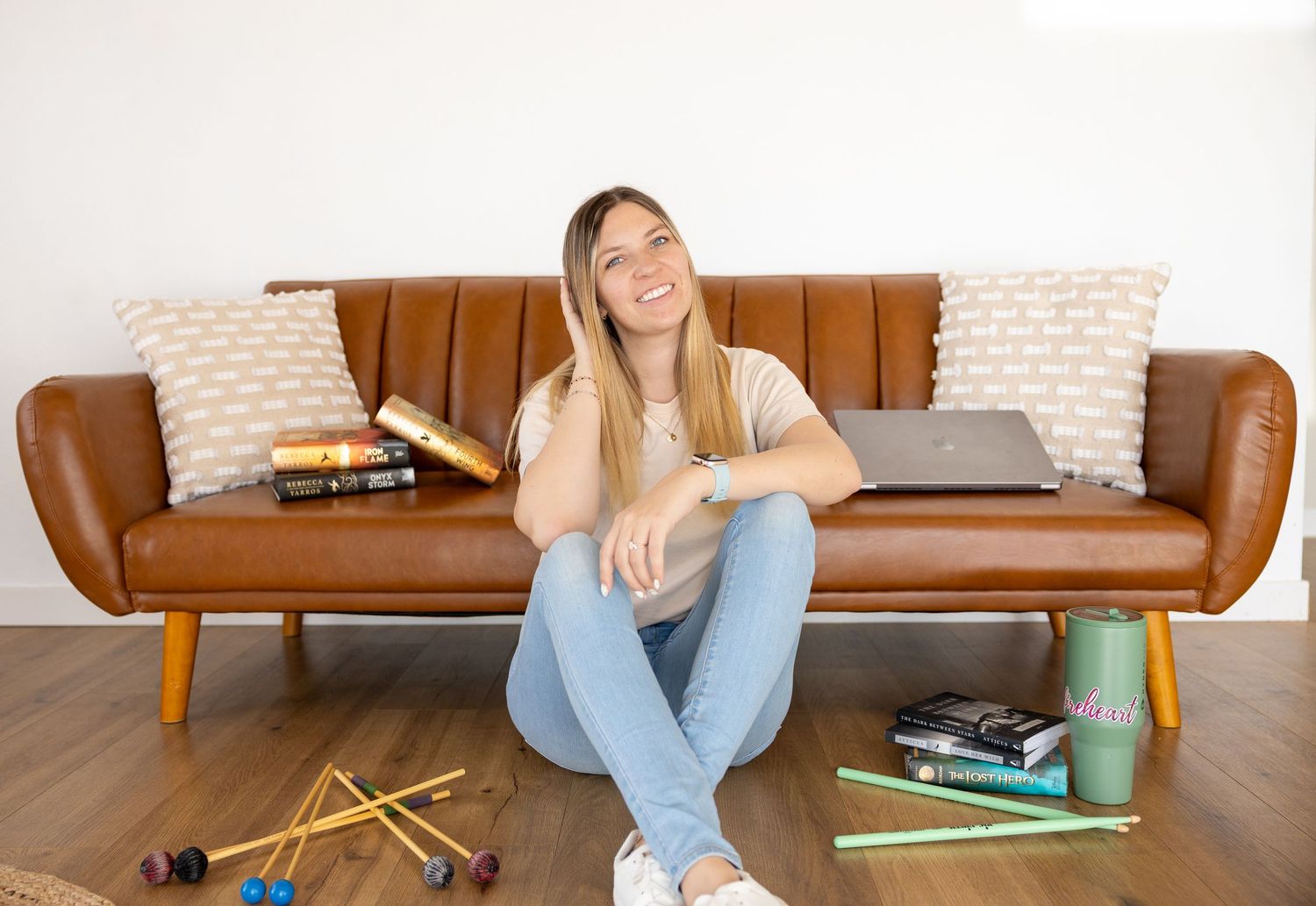 A girl is sitting in front of a couch with drumsticks, books, cameras, and her computer for some photography branding photos.