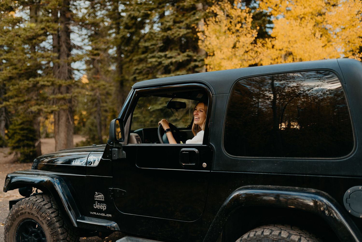 A girl is smiling out her window while driving her beautiful black Jeep Wrangler.