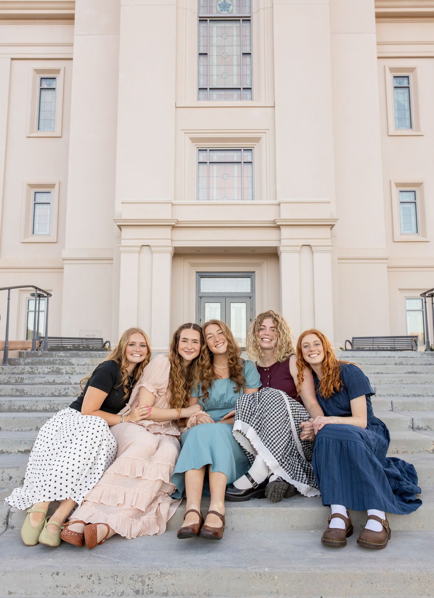 A group of 5 girls are sitting on the steps of the LDS Temple in Cedar City, Utah, snuggled up next to each other.