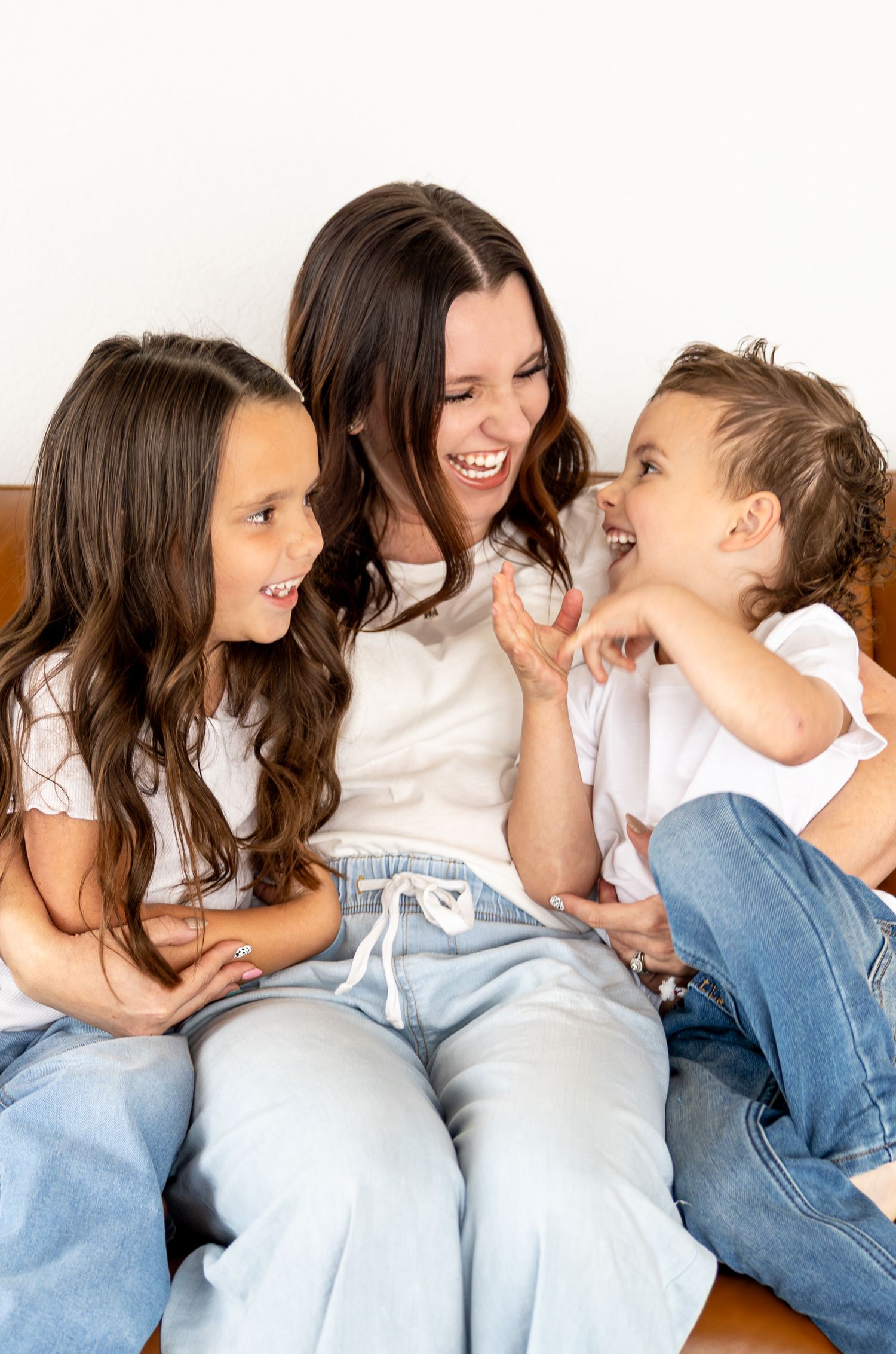 A mom is tickling and laughing with her son and daughter.