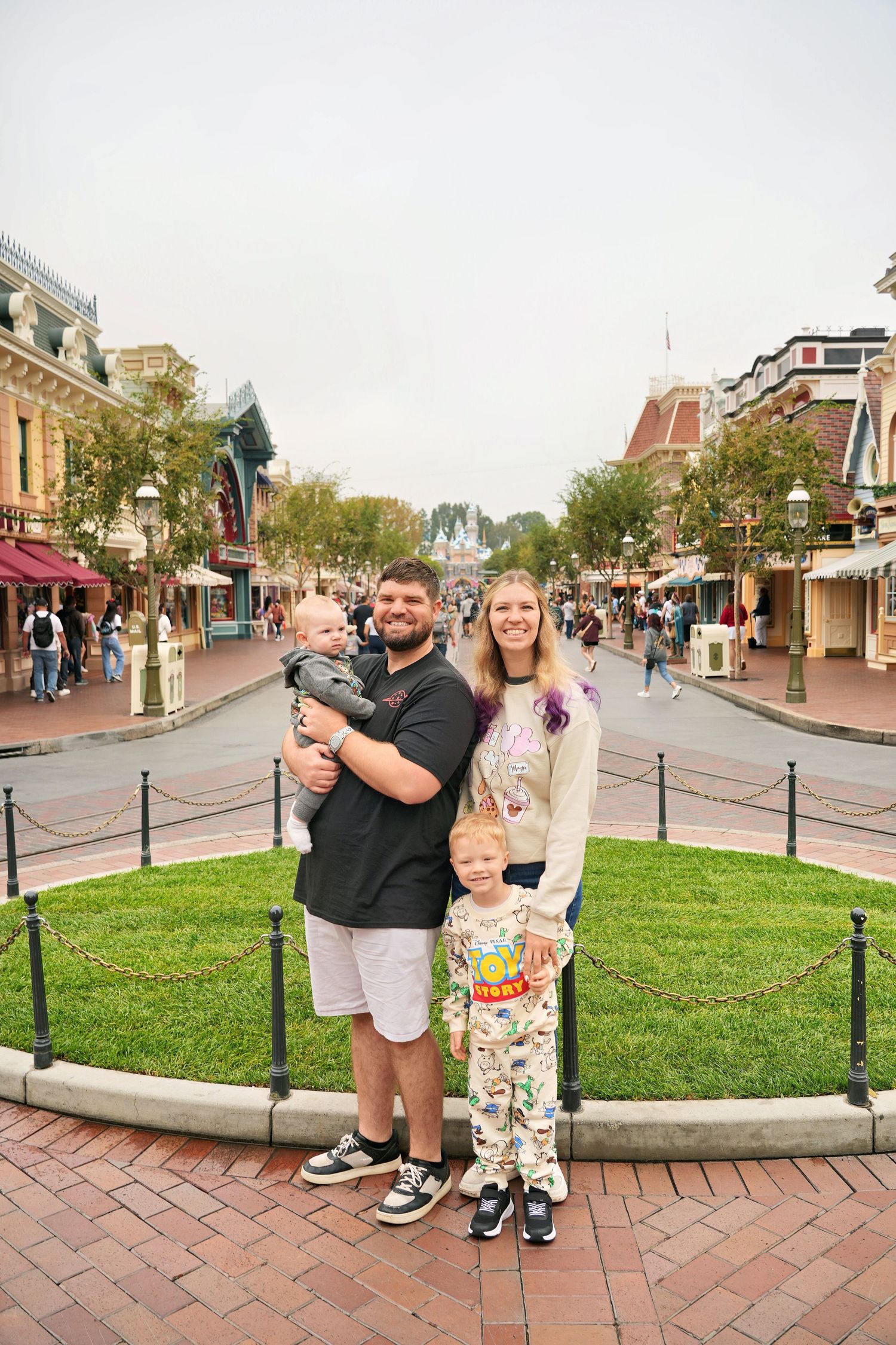 A small family is smiling together in front of the Disneyland Castle.