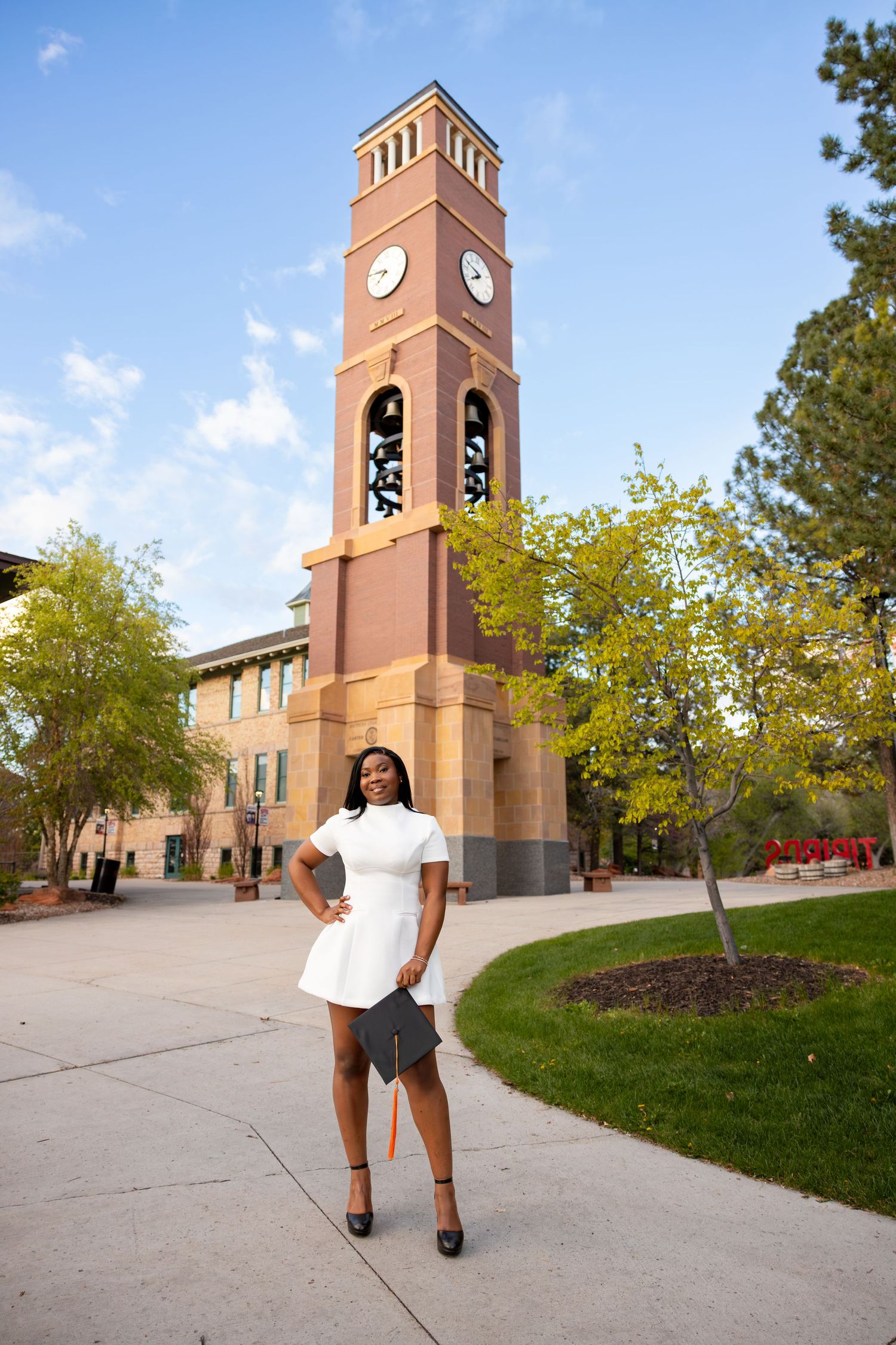 A college graduate is holding her cap in front of the SUU Bell Tower in Southern Utah.