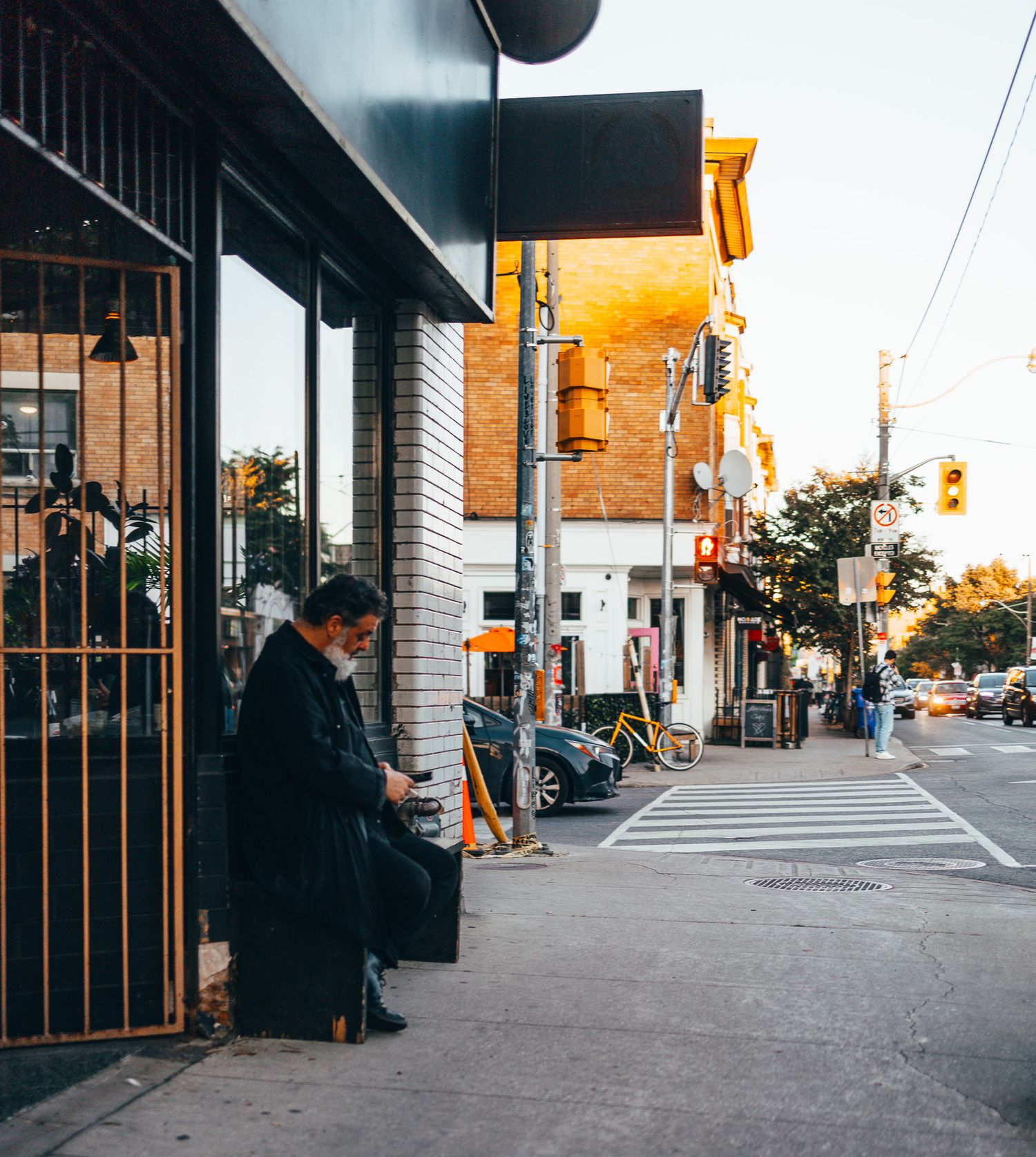 Empty urban sidewalk with storefronts and traffic signals at sunset.
