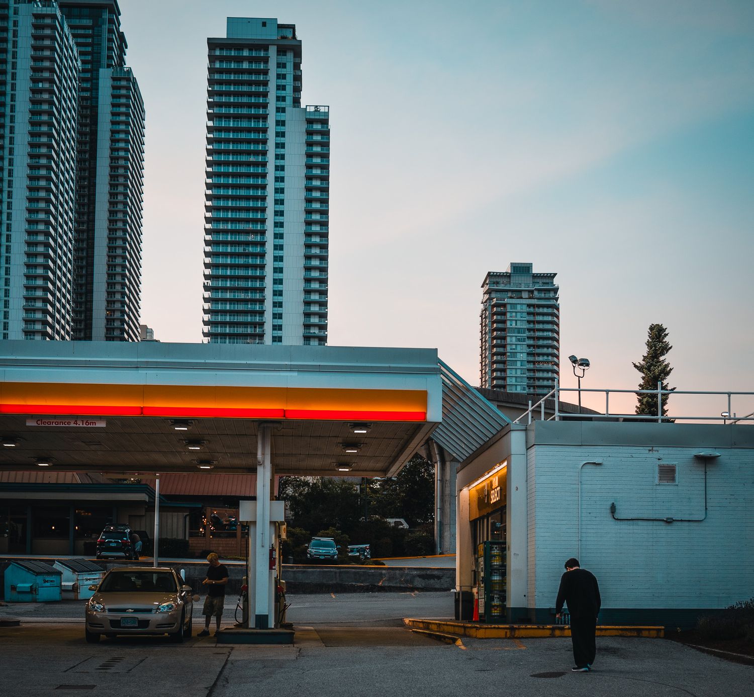 Modern high-rise buildings and gas station at dusk in an urban setting.