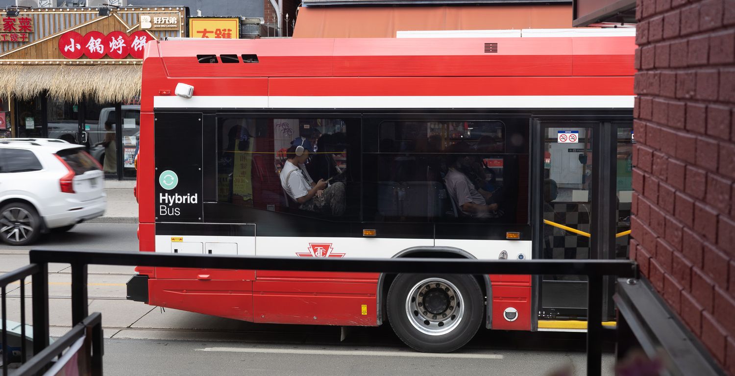Row of red public transit buses parked along city street.