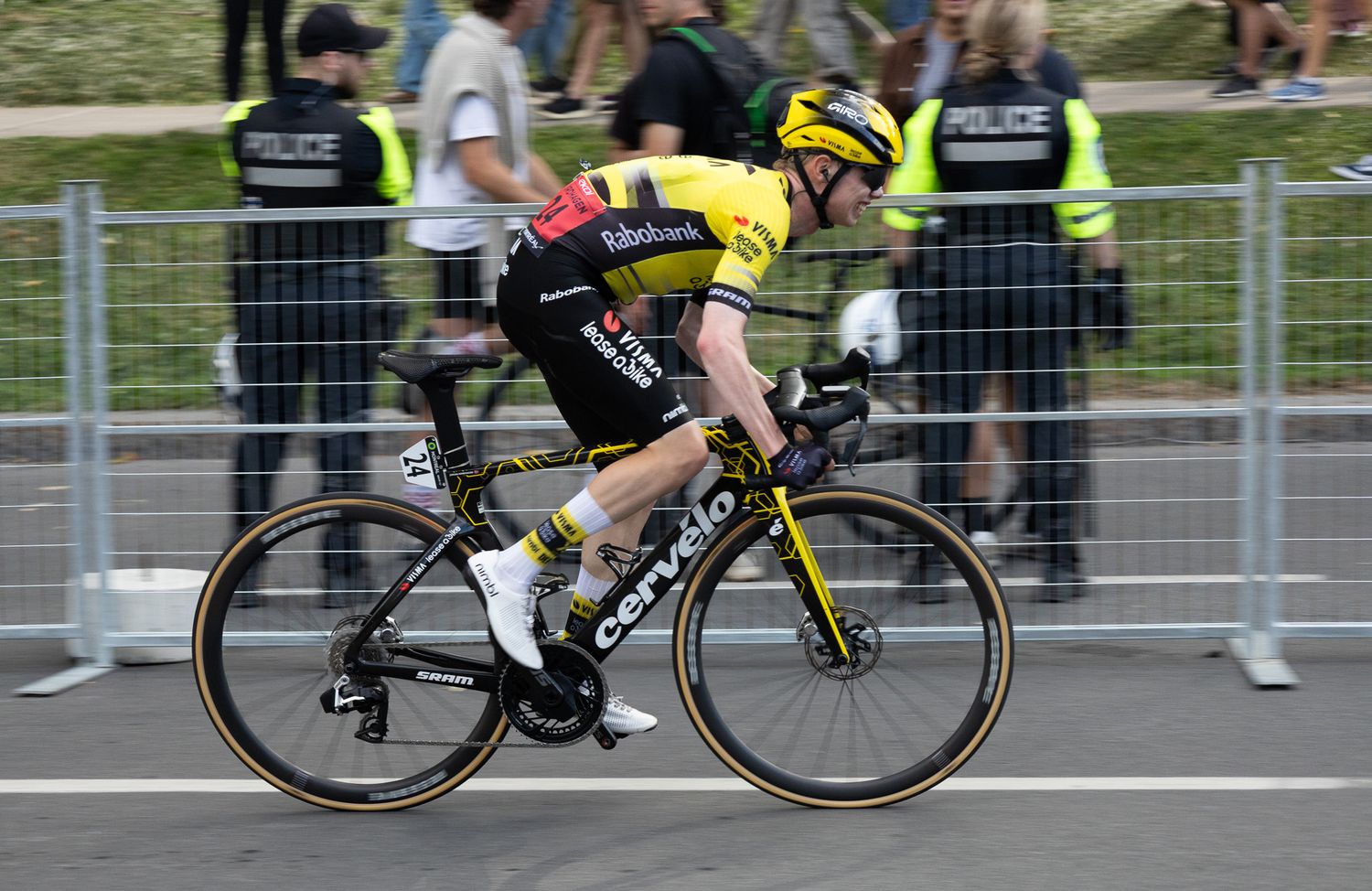 Cyclist in yellow racing gear pedals aggressively on road bike during competition.