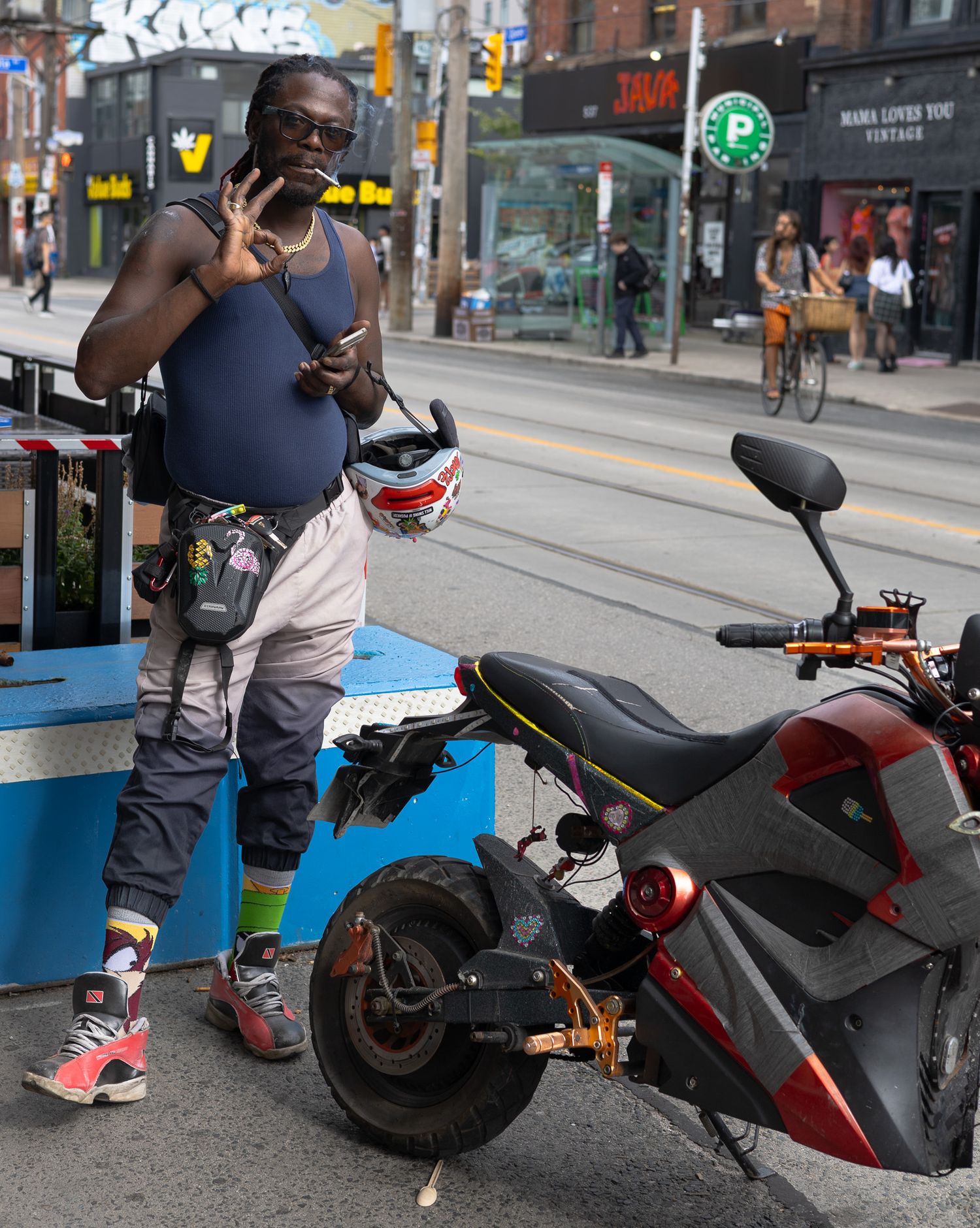 A person parks a red and black electric scooter on a city sidewalk near a bike rack.
