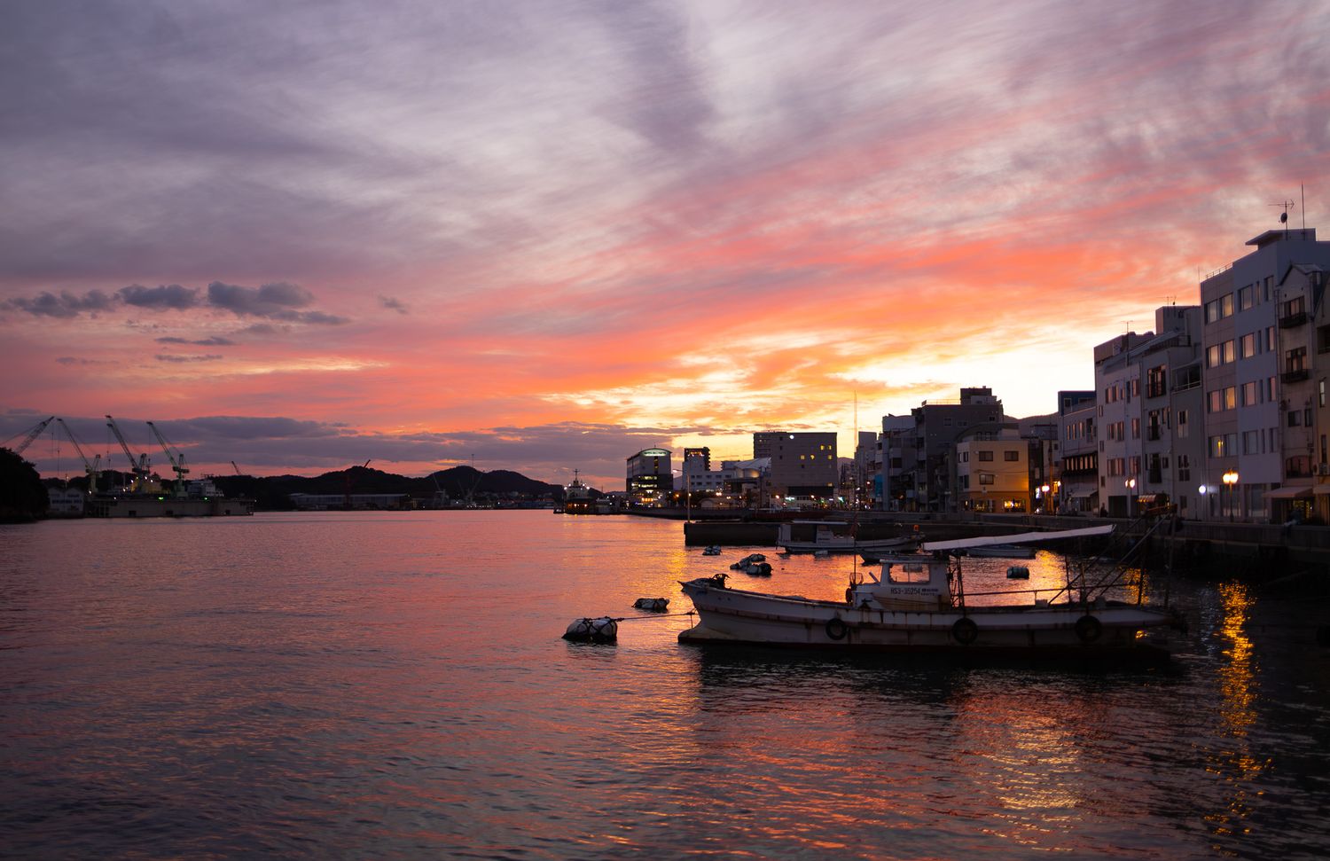 Dramatic sunset over a harbor with boats silhouetted against the colorful sky.
