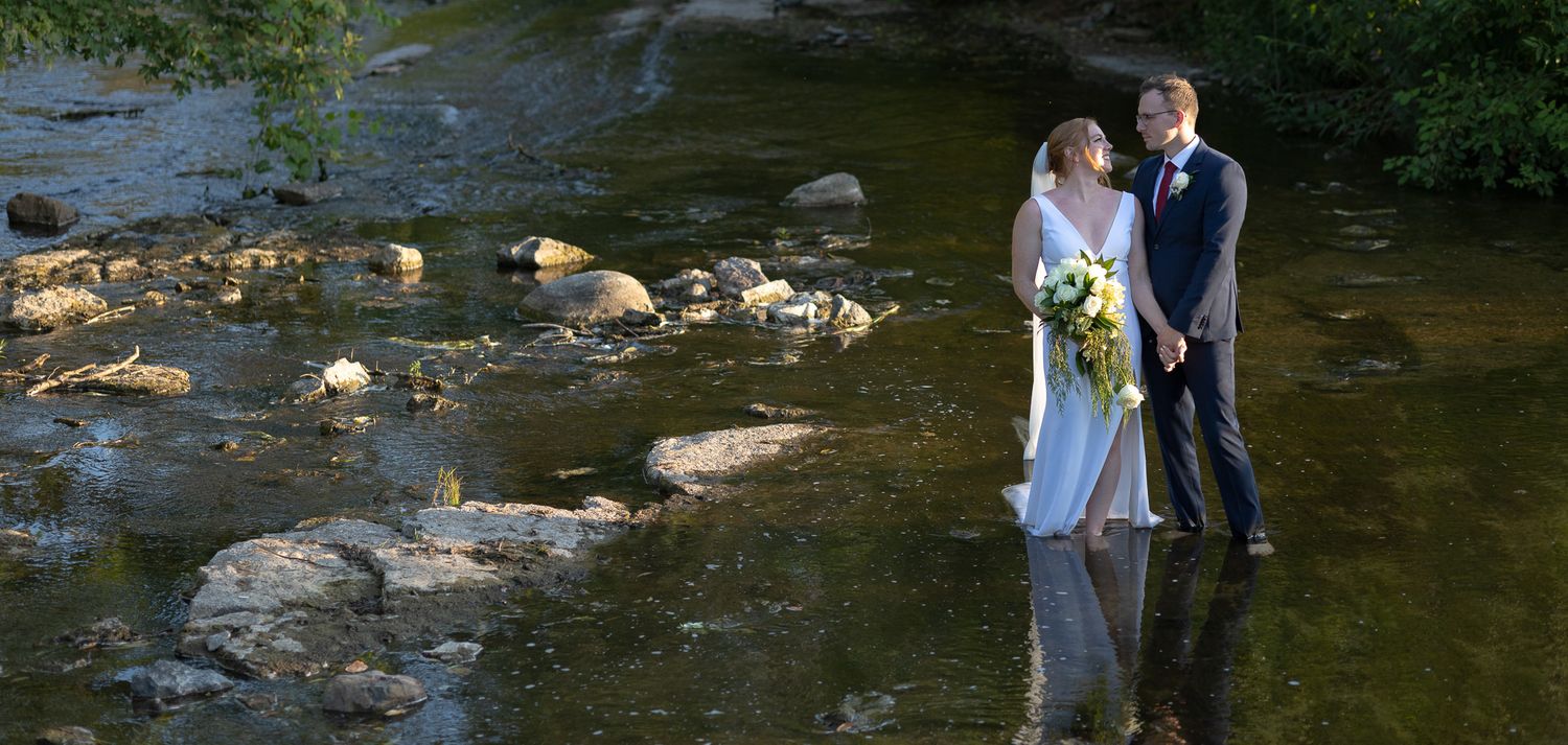 Wedding couple posing near rocky stream in natural outdoor setting.