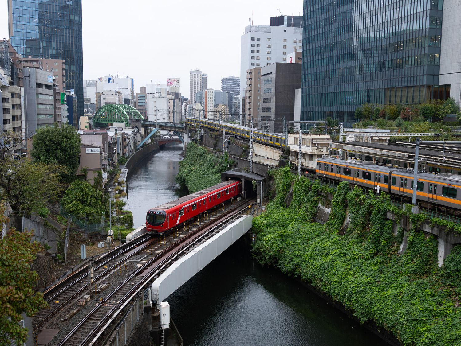 Urban railway tracks running alongside modern buildings and lush greenery in a city setting.
