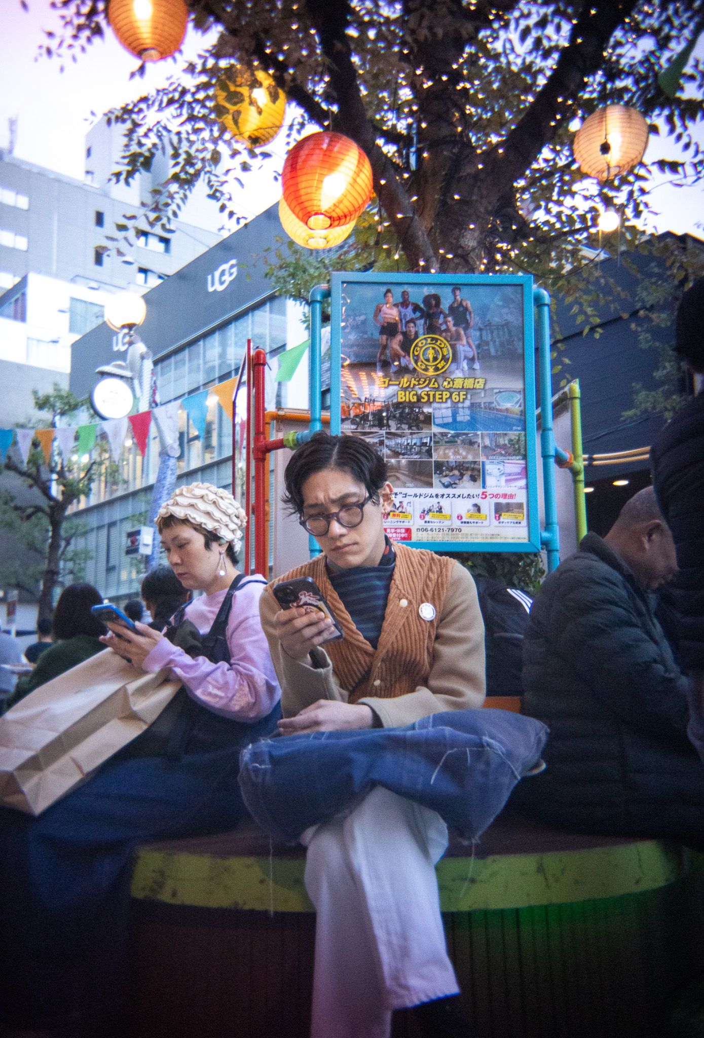 People relaxing on outdoor benches under glowing paper lanterns at dusk.