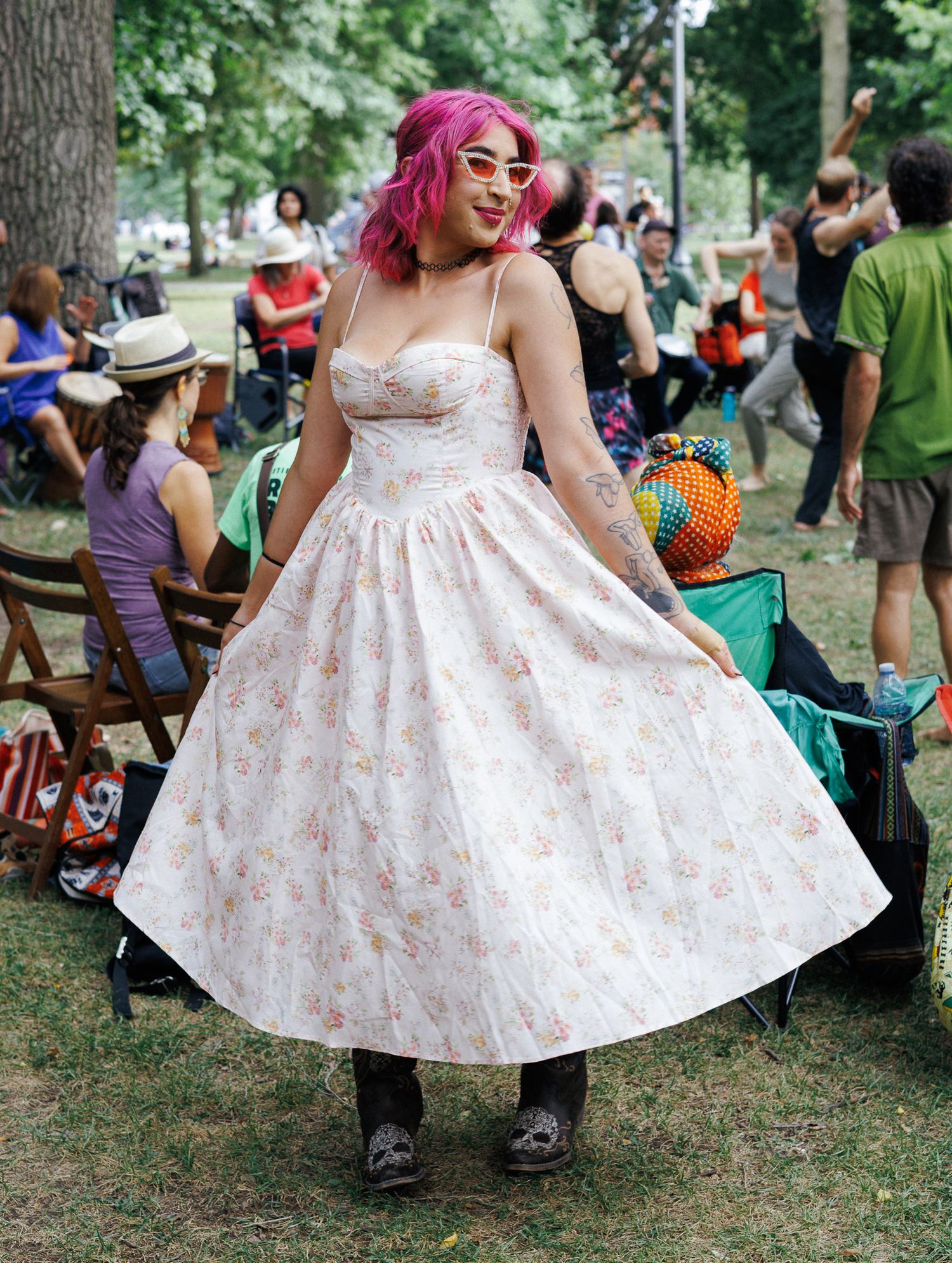 A person in a floral white dress twirls playfully in a park setting during a summer gathering.
