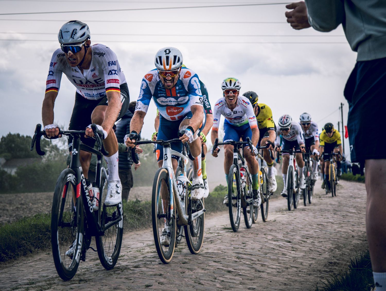 Peloton of cyclists racing on cobblestone road during professional cycling event.