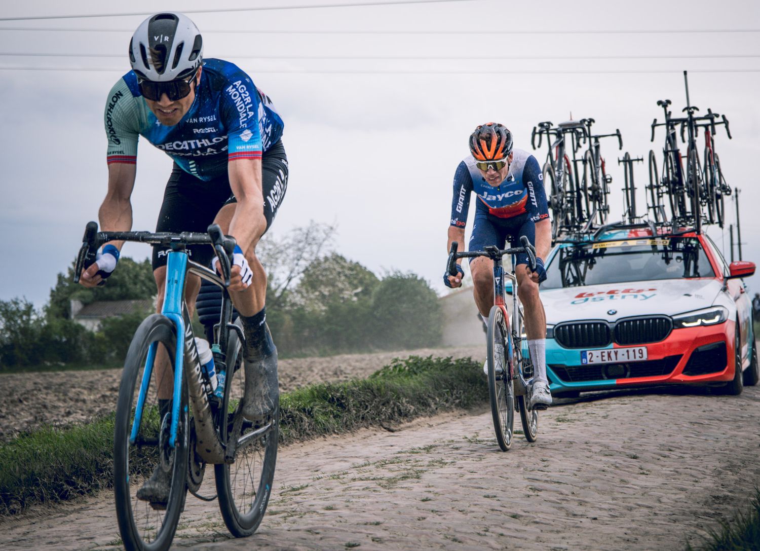 Cyclists navigate dusty gravel road with support vehicle following behind.