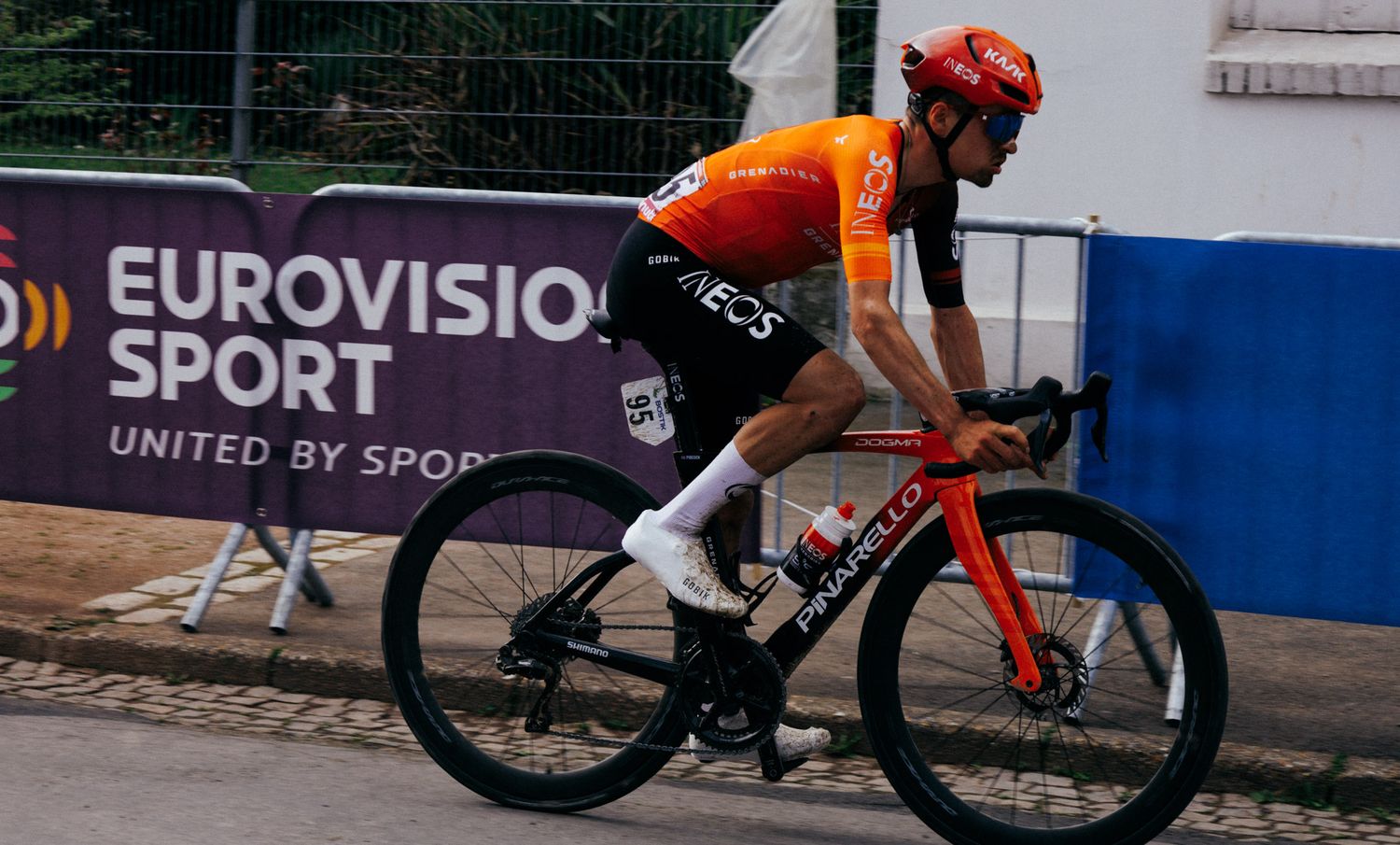 Cyclist in orange jersey races past Eurovision Sport branded barrier.