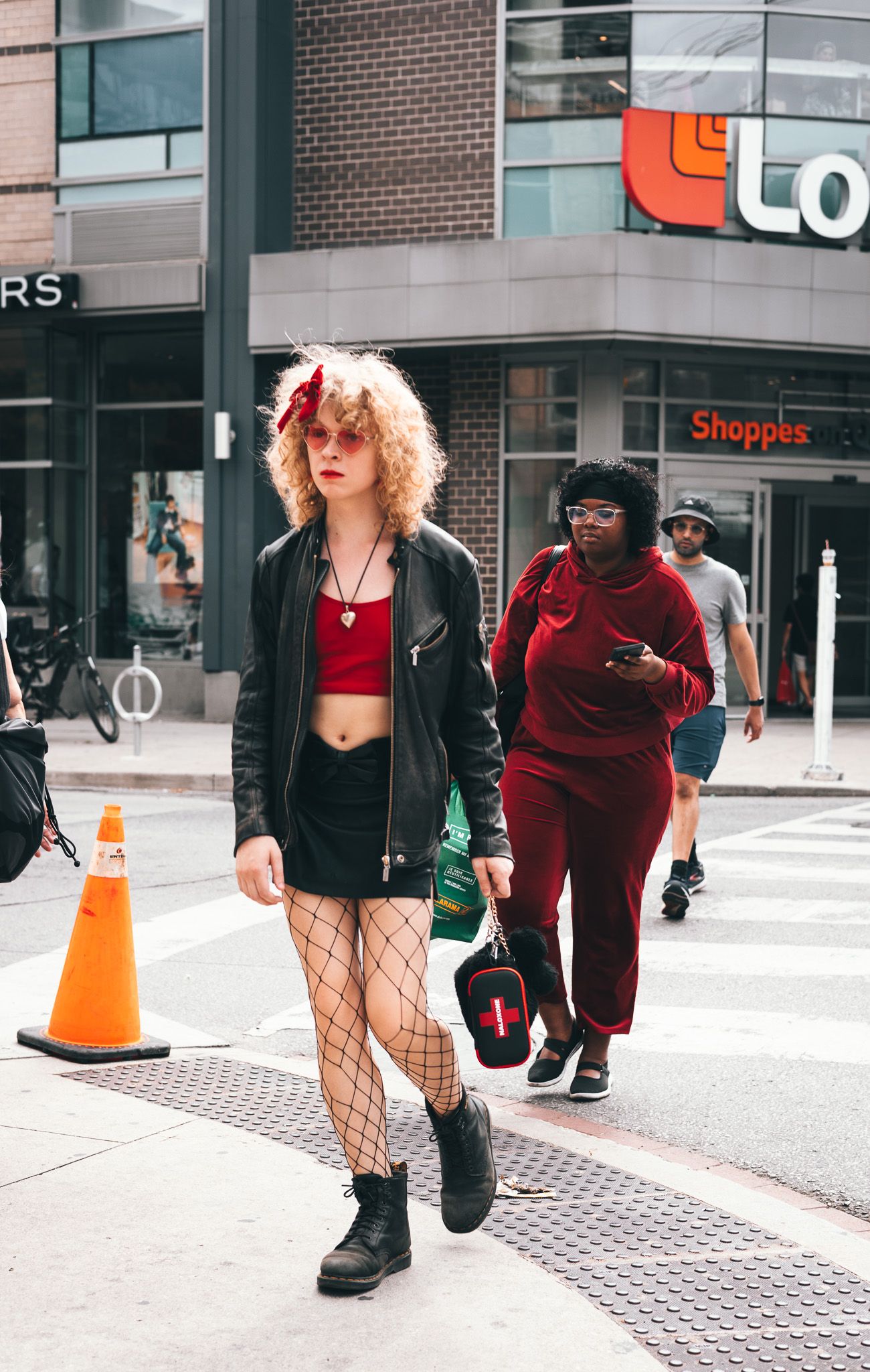 Two people in red and black outfits walk past a retail storefront on a city sidewalk.