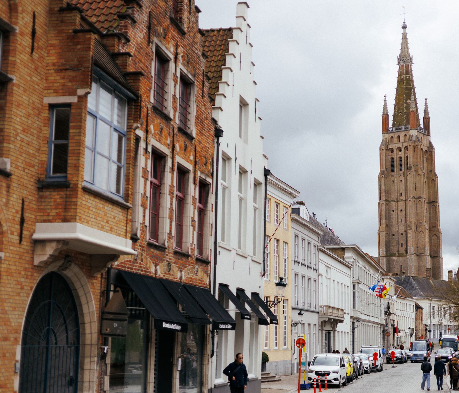 Historic brick buildings and church spire along a quiet European street.