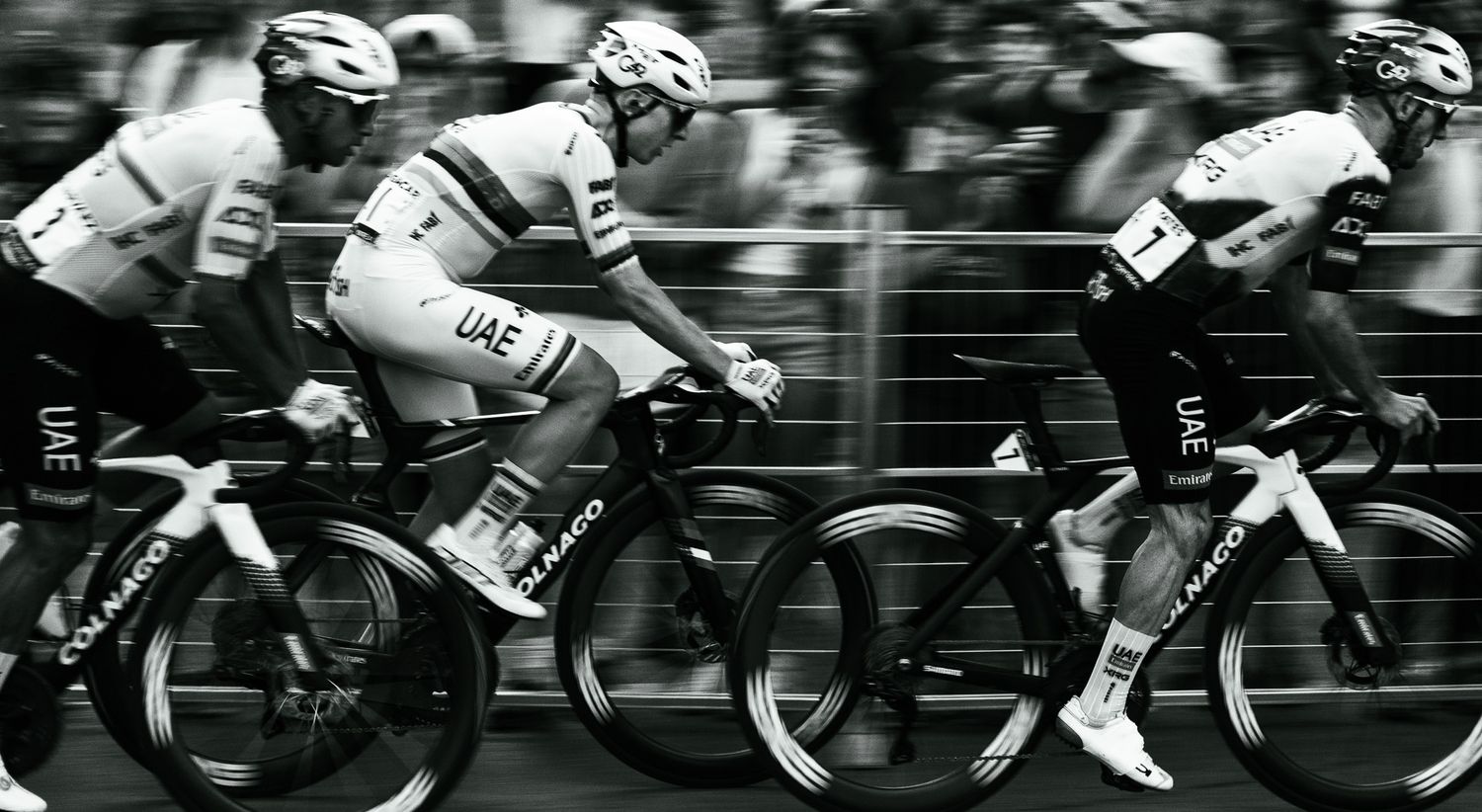 Black and white image of cyclists racing in a tight pack during a competitive road race.