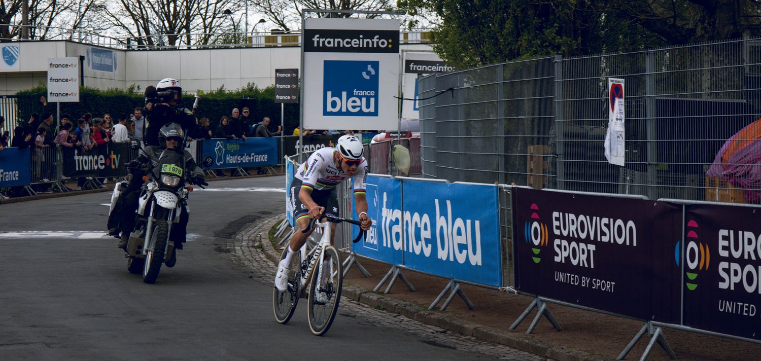 Cyclist races past France Bleu sponsored barriers during professional competition.