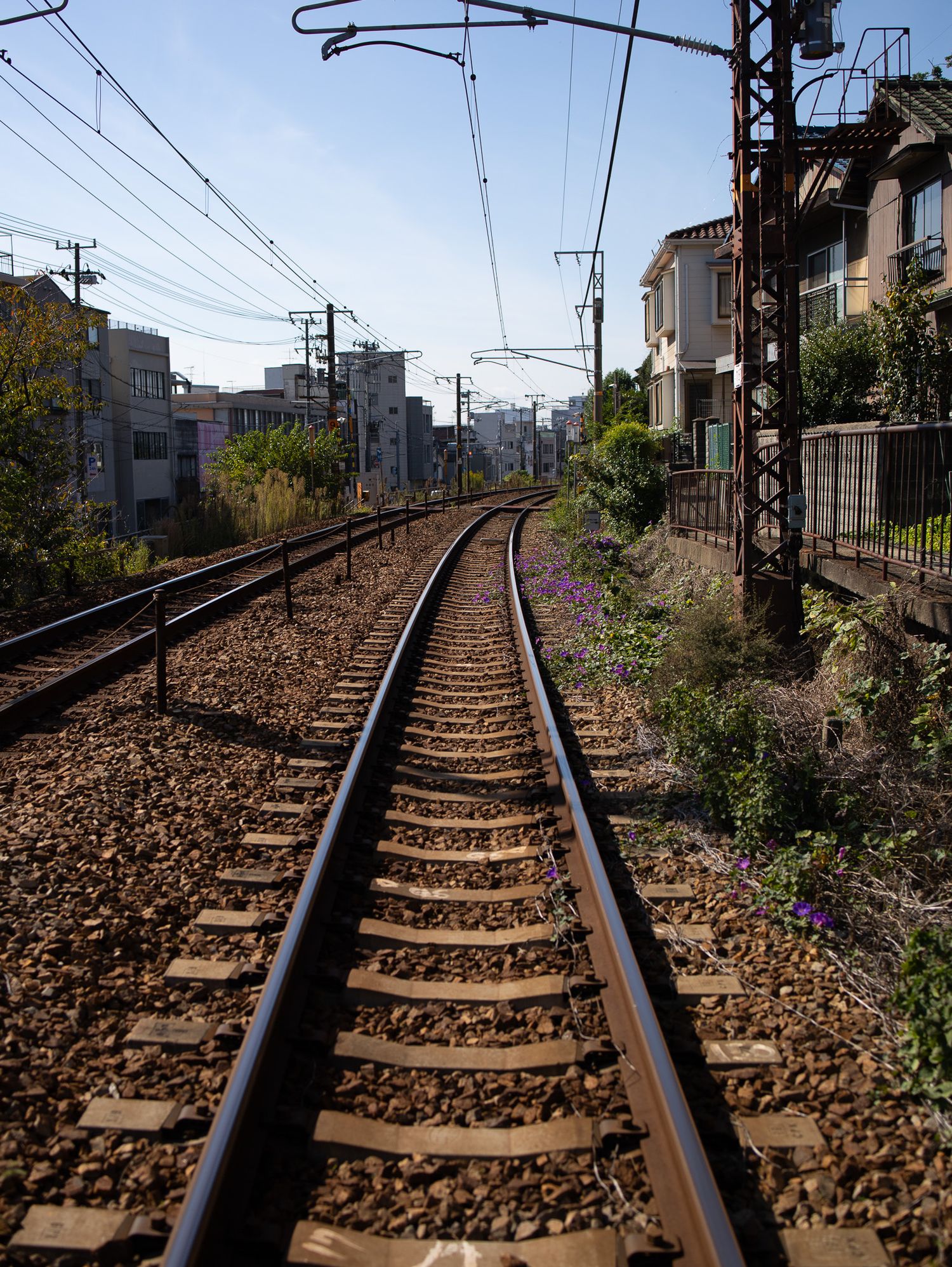 Railroad tracks stretching into the distance with power lines and urban buildings alongside.