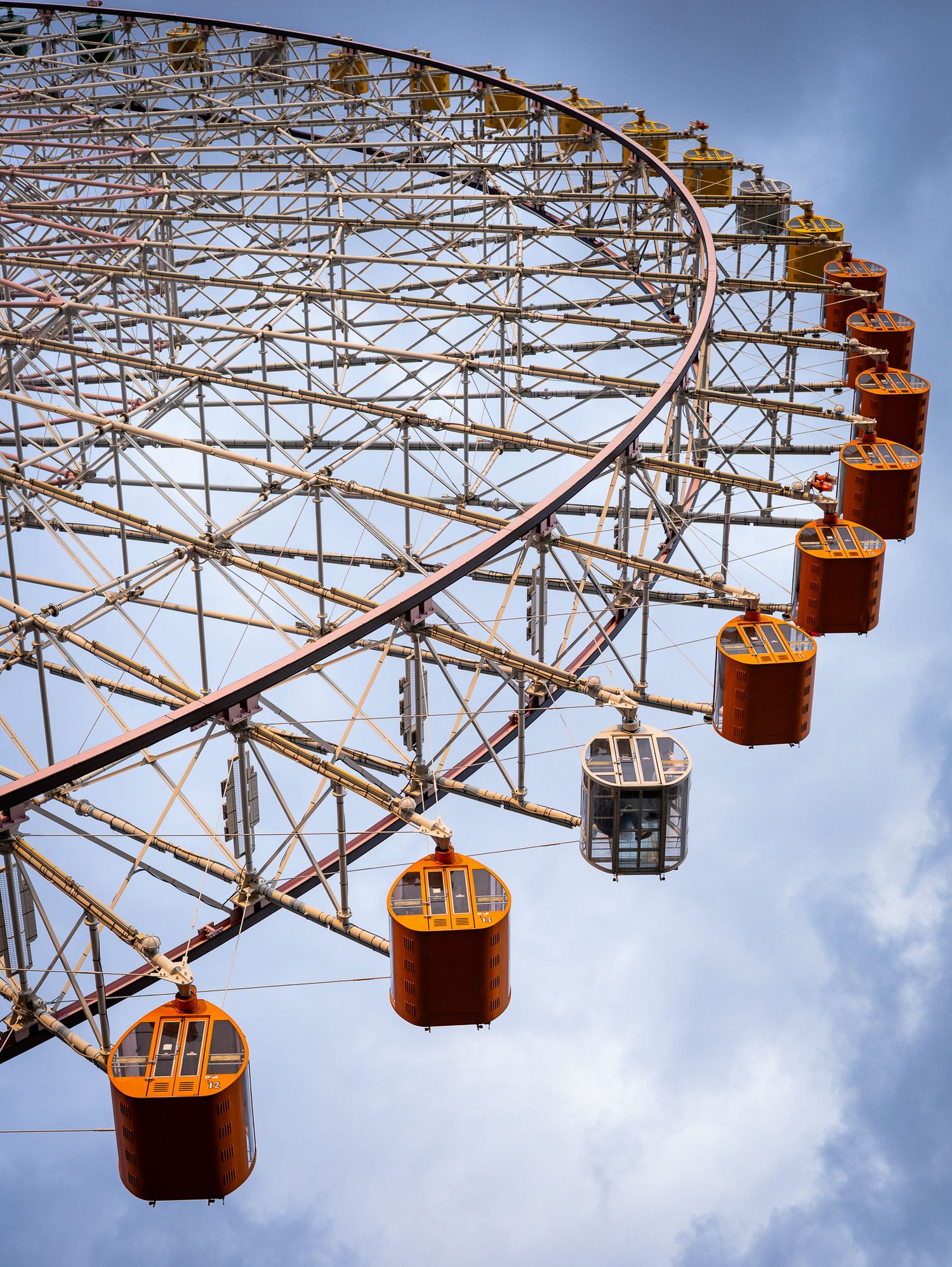 Orange gondolas of a Ferris wheel against blue sky viewed from below.