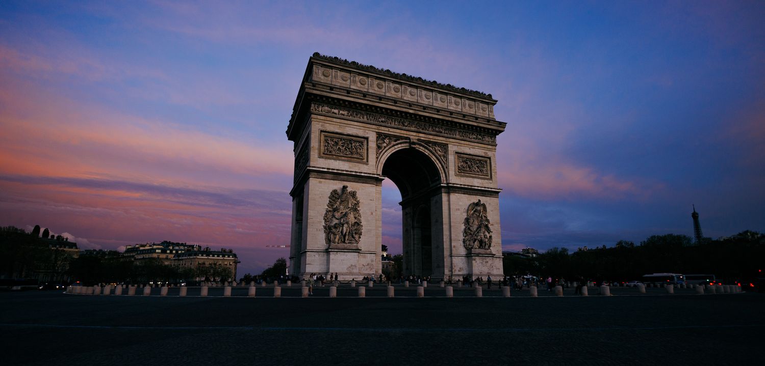 Silhouette of Arc de Triomphe against dramatic sunset sky in Paris.