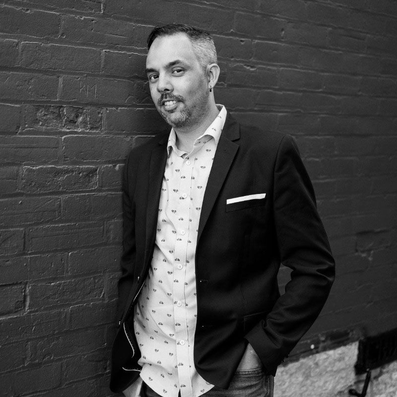 Black and white portrait against a brick wall showing formal attire and classic styling.