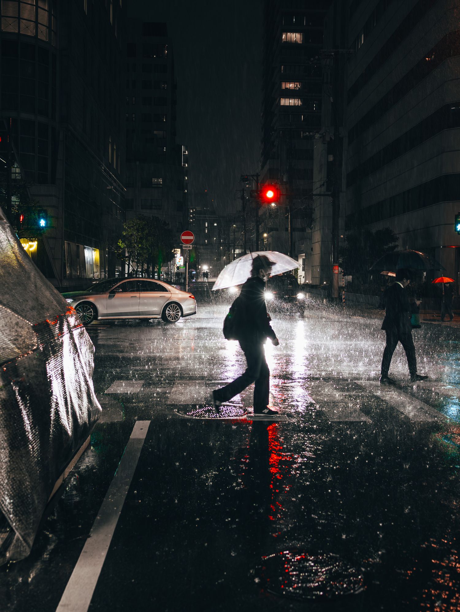 Silhouettes of pedestrians walking in heavy rain at night on a city street.