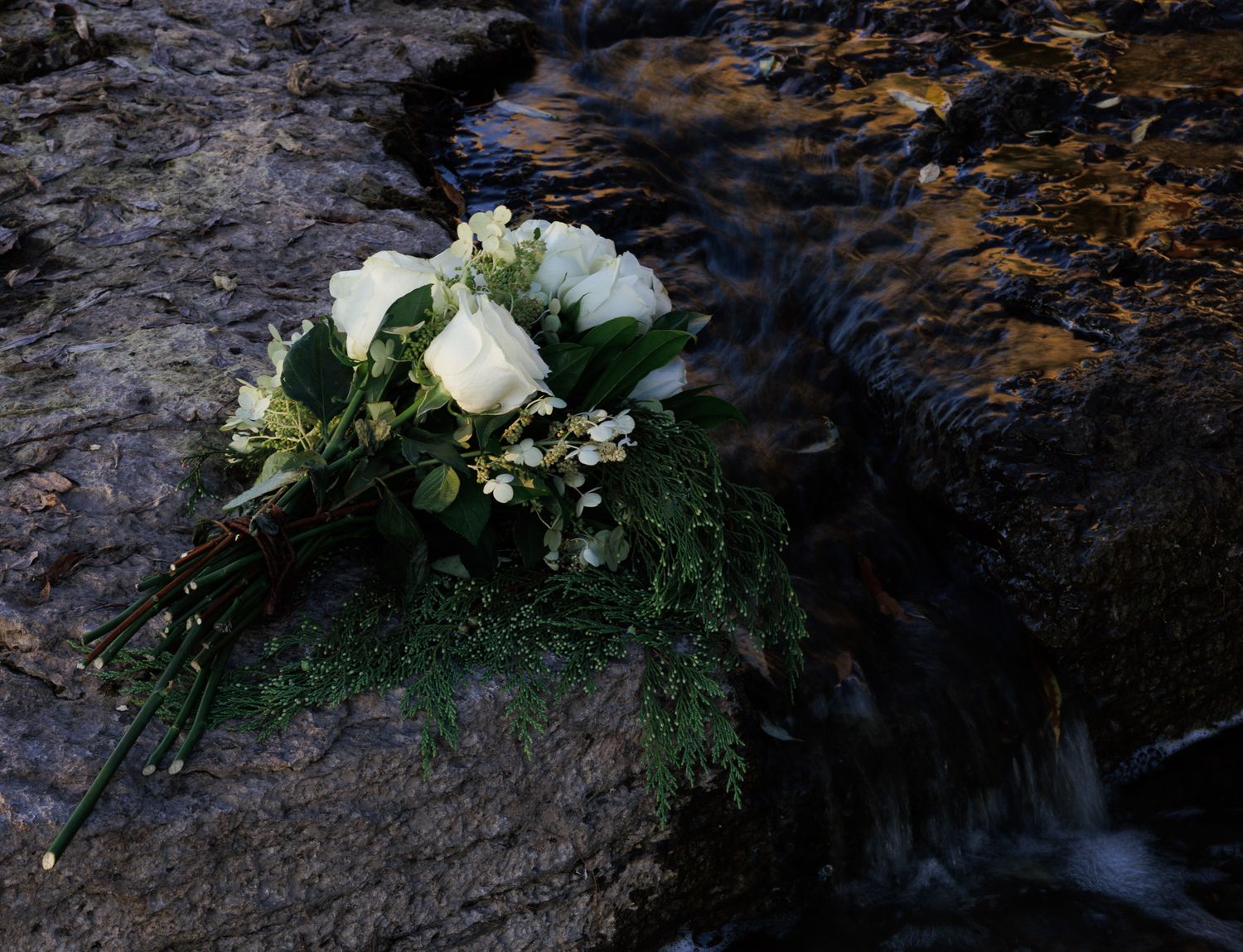 White floral arrangement placed on dark rocky surface near water.