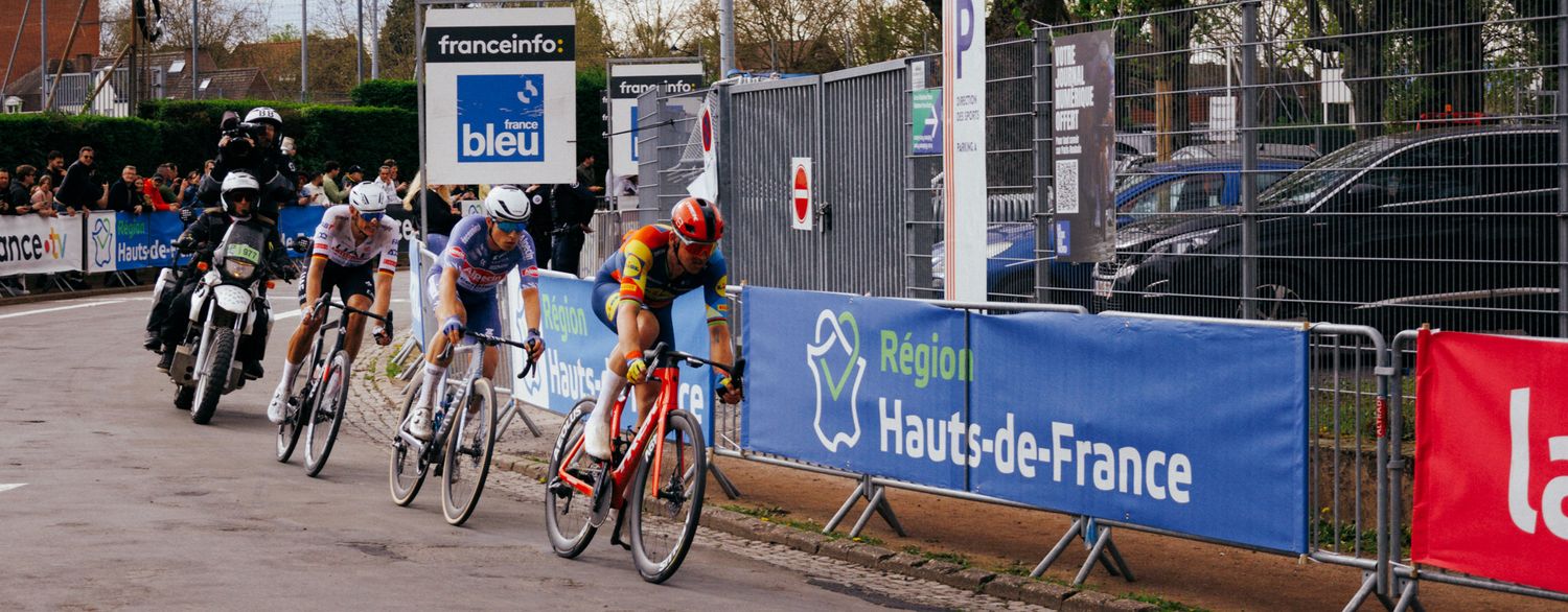 Professional cyclists racing at high speeds on a road course during a competitive cycling event.