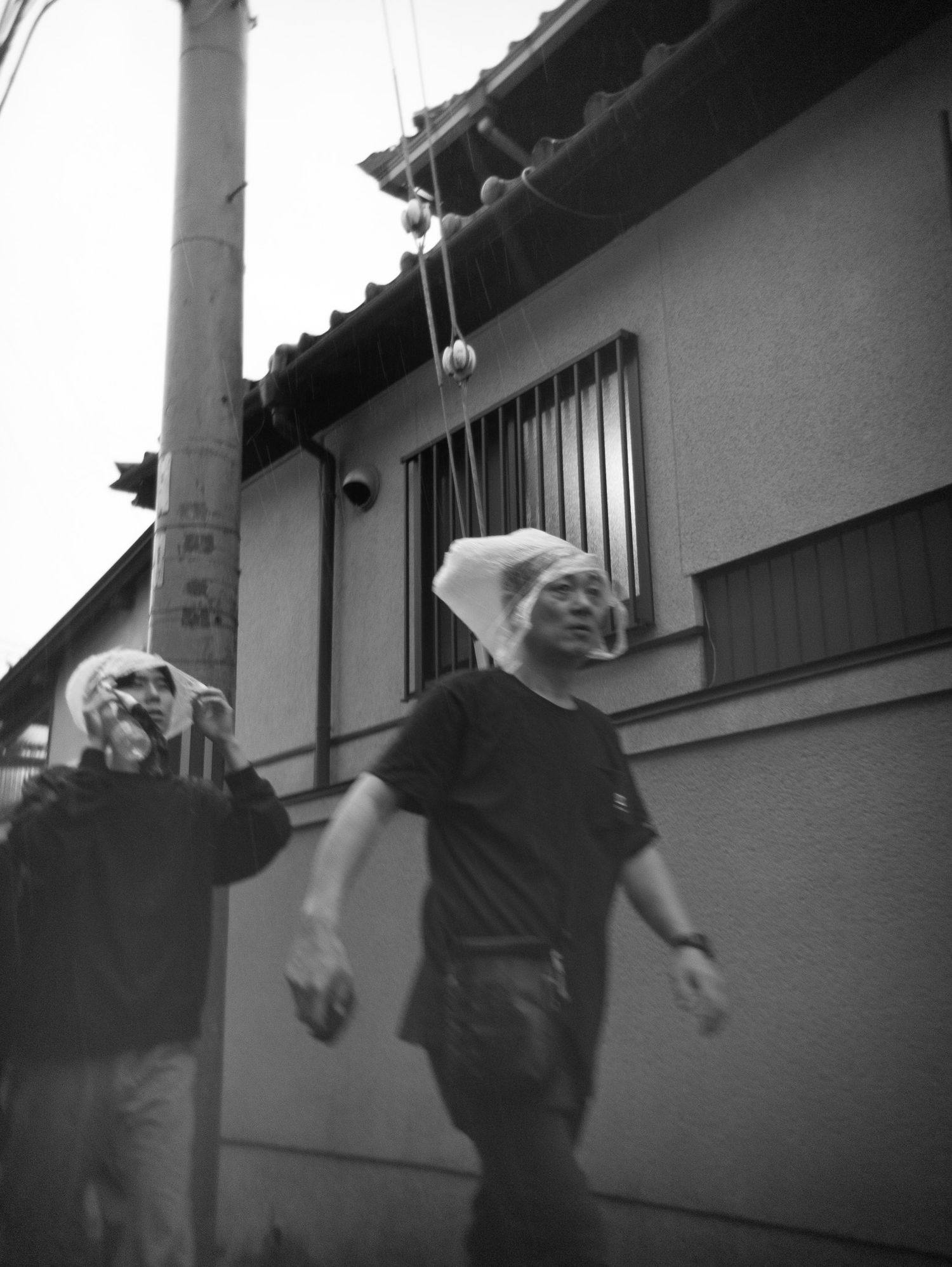 Black and white image of figures moving past a white wall in an artistic composition.