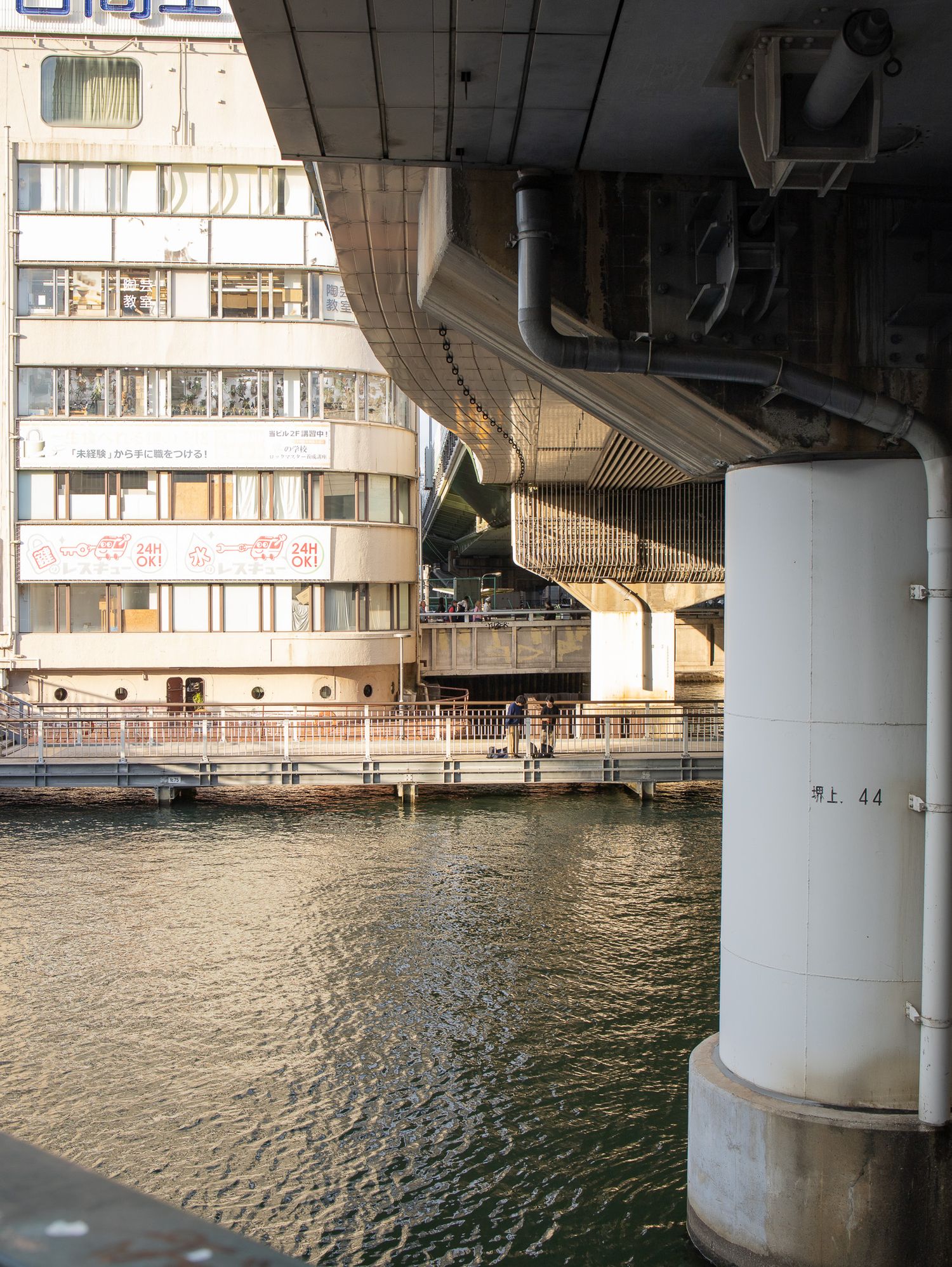 View under a concrete bridge showing support columns and rippling water below.