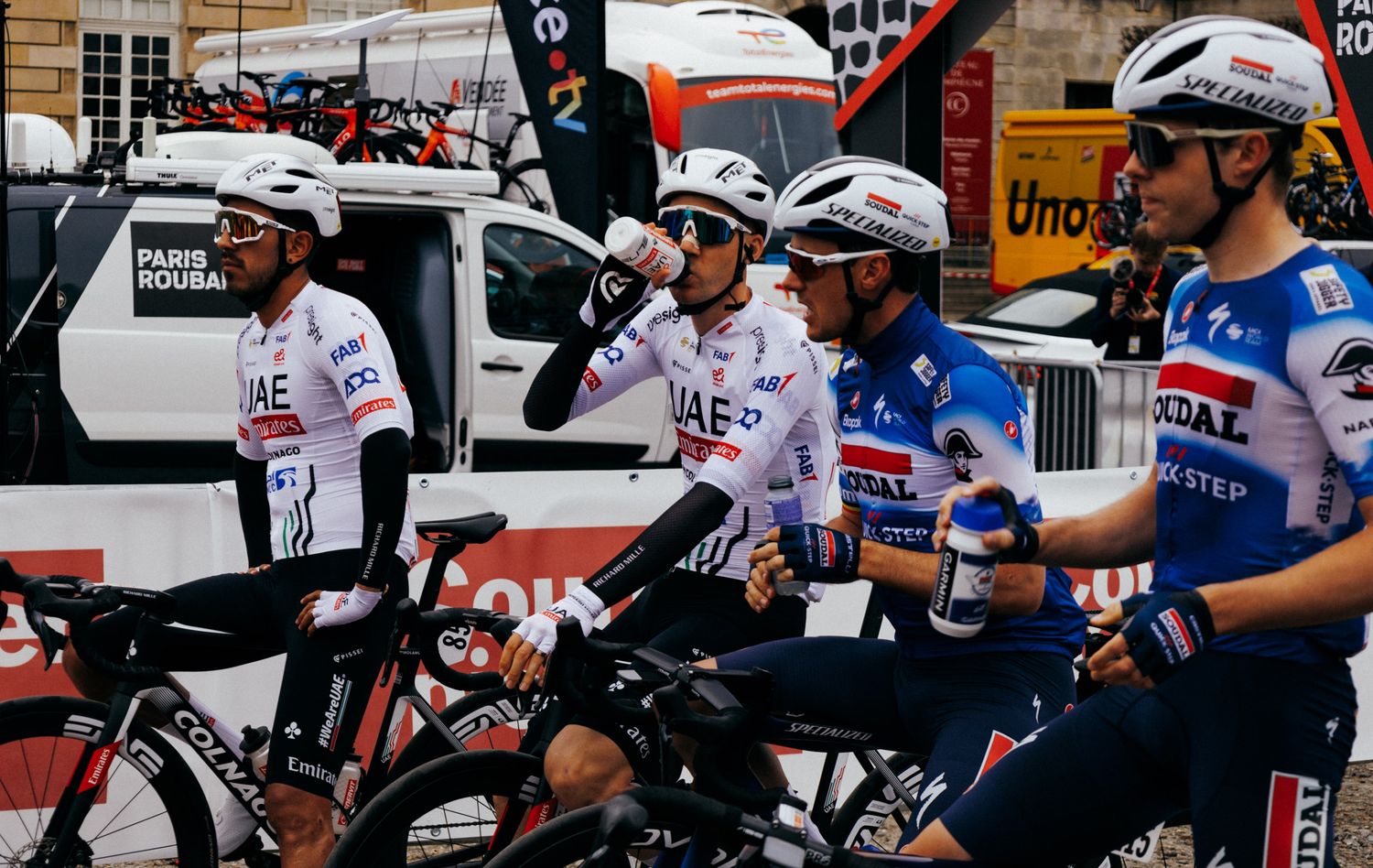 Group of cyclists in white jerseys hydrating during race break.
