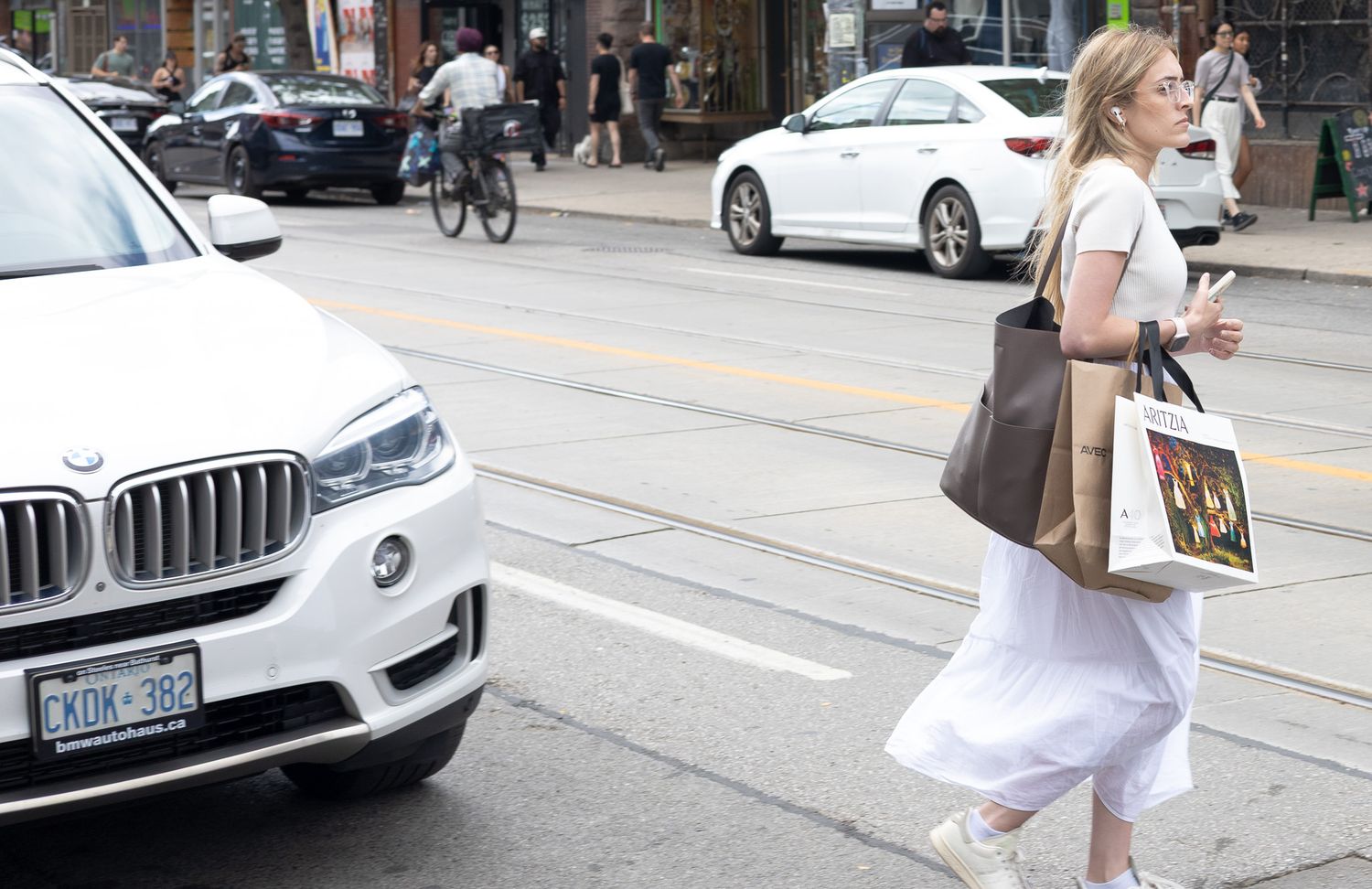 A person in a light summer dress walks past parked cars on an urban street.