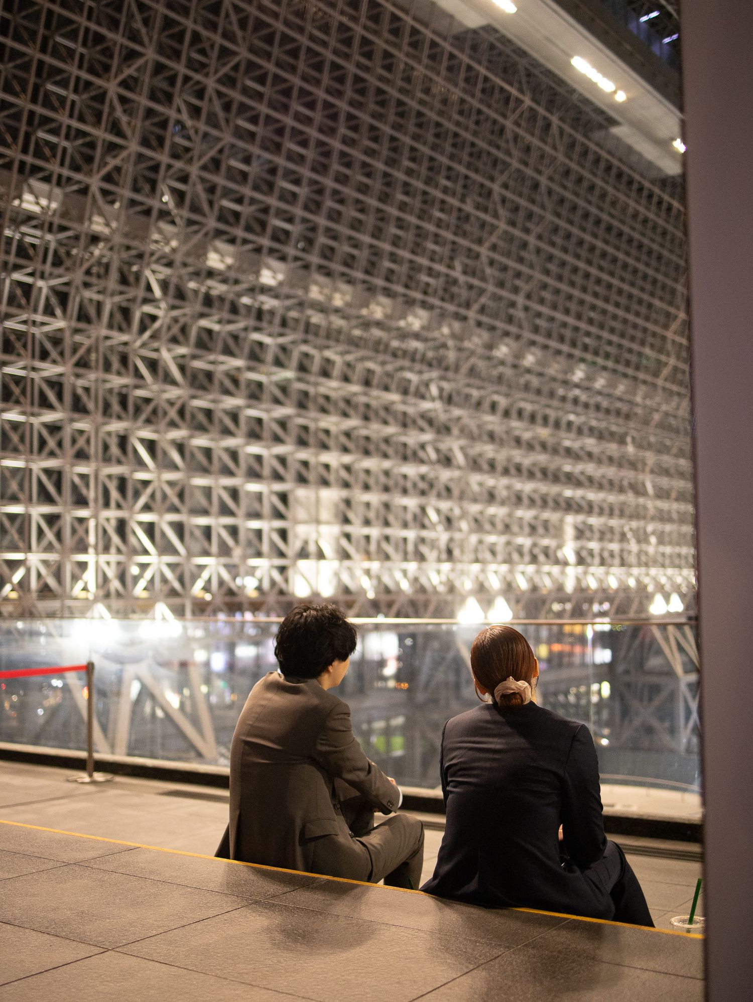 People sitting under a large geometric ceiling structure in a modern architectural space.