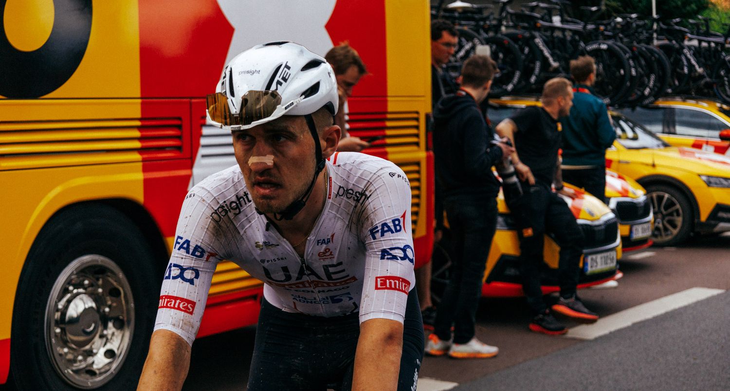 Cyclist rests near yellow team bus during professional cycling event.