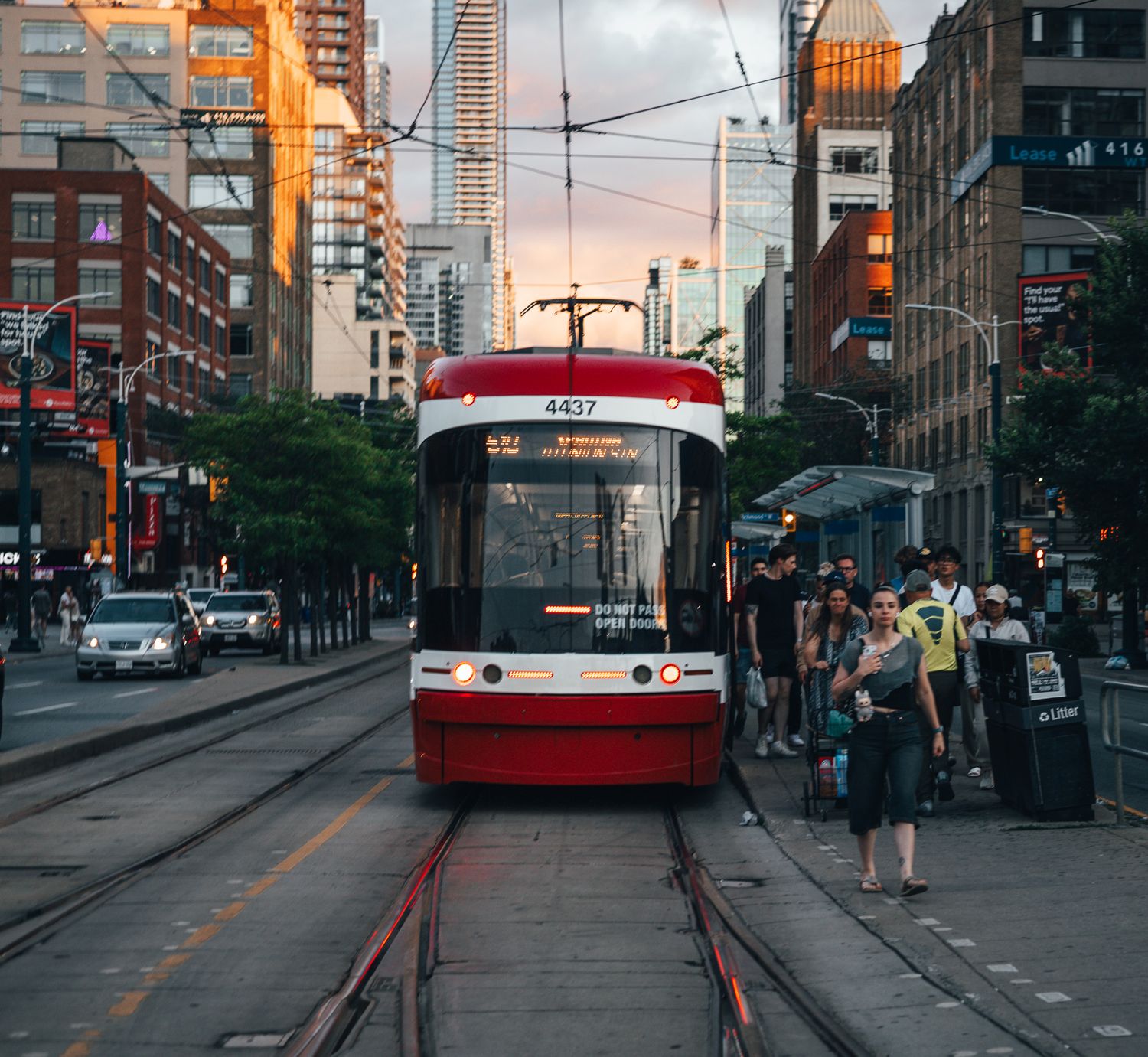 A red and white streetcar stops on tracks in downtown Toronto at sunset with modern buildings in the background.